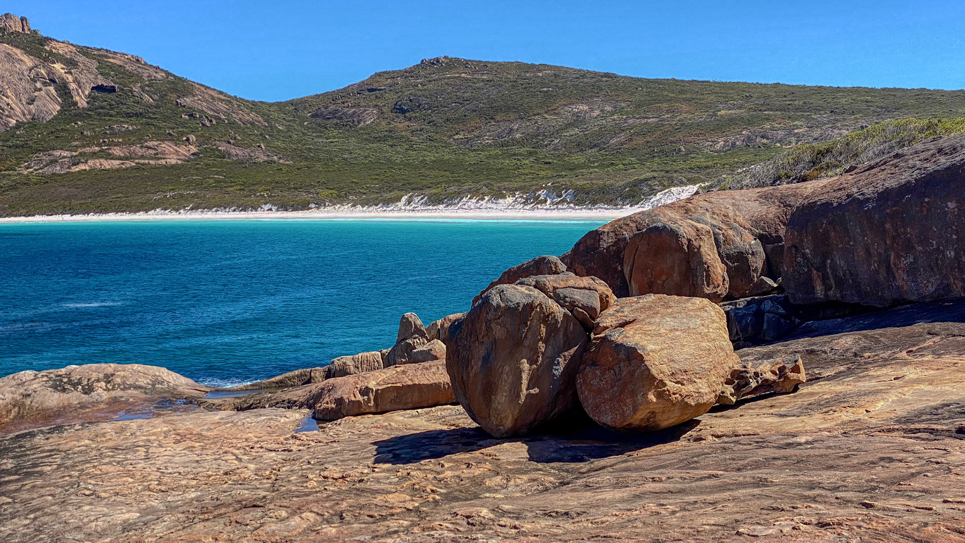 A rugged coastal landscape showcases weathered boulders, a serene ocean, and lush hills, evoking tranquility and adventure in nature.