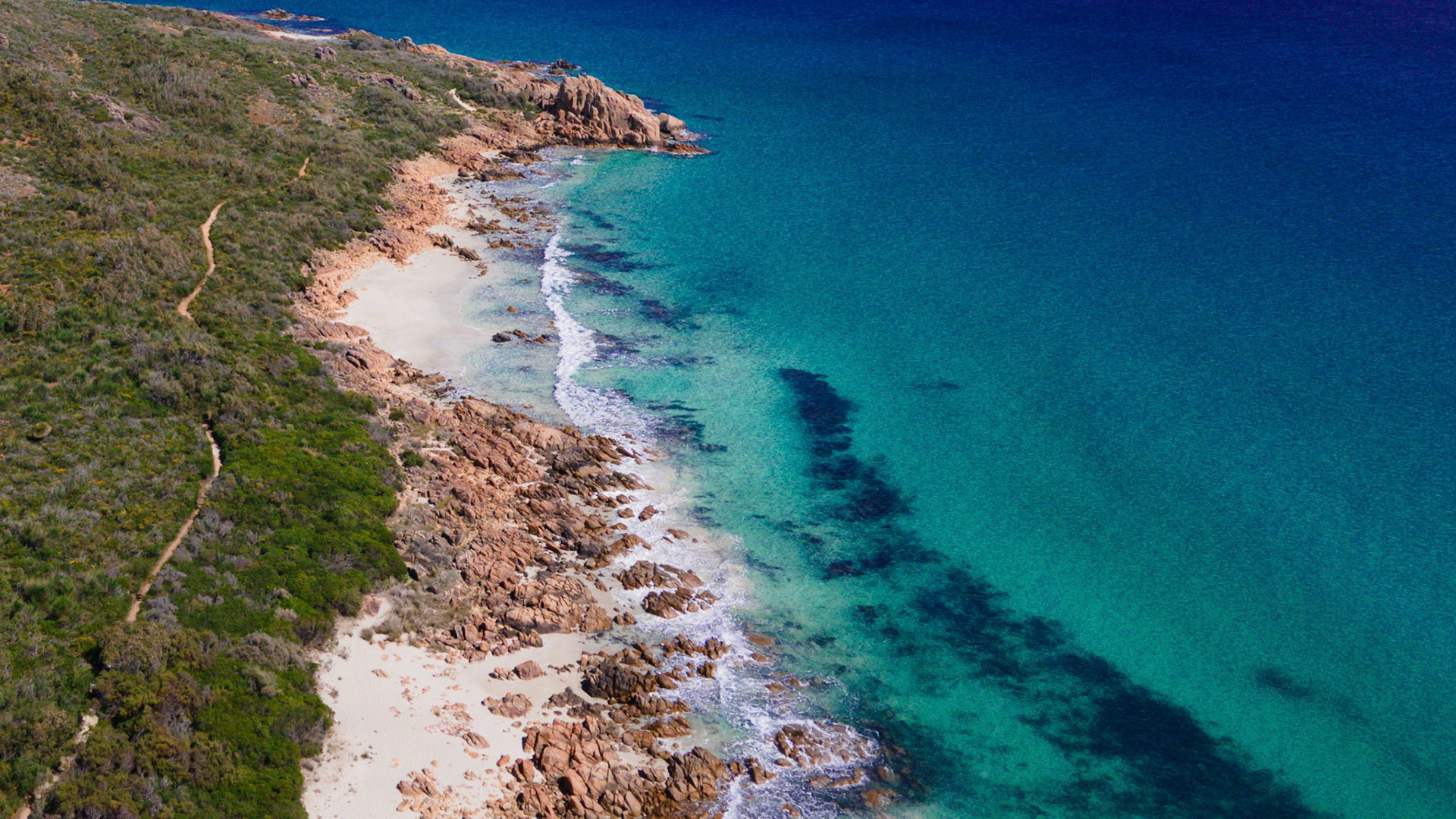 A stunning aerial photograph capturing a rugged coastline with contrasting textures of rocky outcrops and lush greenery. The clear turquoise waters gently lap against the sandy shore, creating a picturesque coastal scene. Ideal for travel and nature themes, showcasing the untouched beauty of the natural landscape.