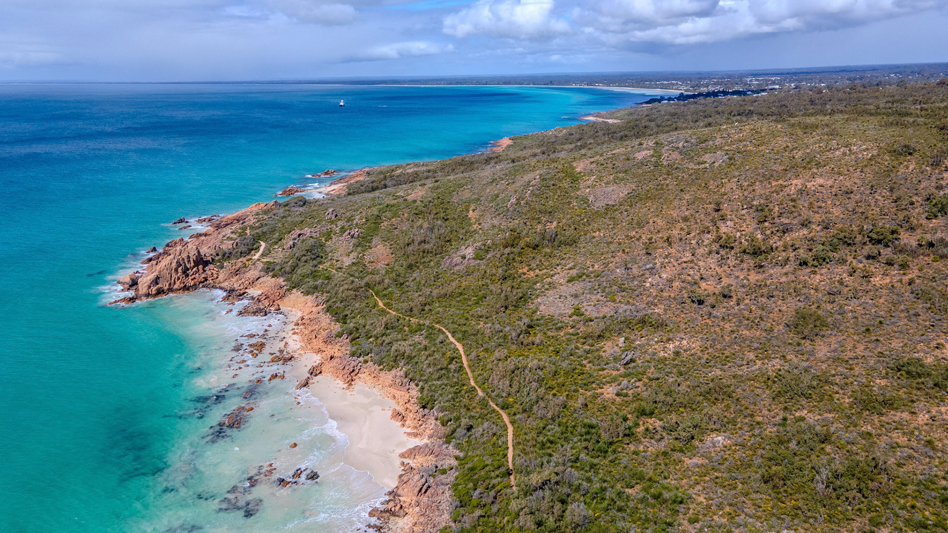 A breathtaking aerial view captures the dramatic coastline with vibrant turquoise waters gently lapping against rugged cliffs. The coastline stretches into the horizon, dotted with lush vegetation and clear skies, creating a picturesque tropical setting ideal for travel and nature enthusiasts. The winding path along the cliffs invites exploration, while the azure sea offers a serene backdrop, embodying the essence of a tranquil coastal escape.