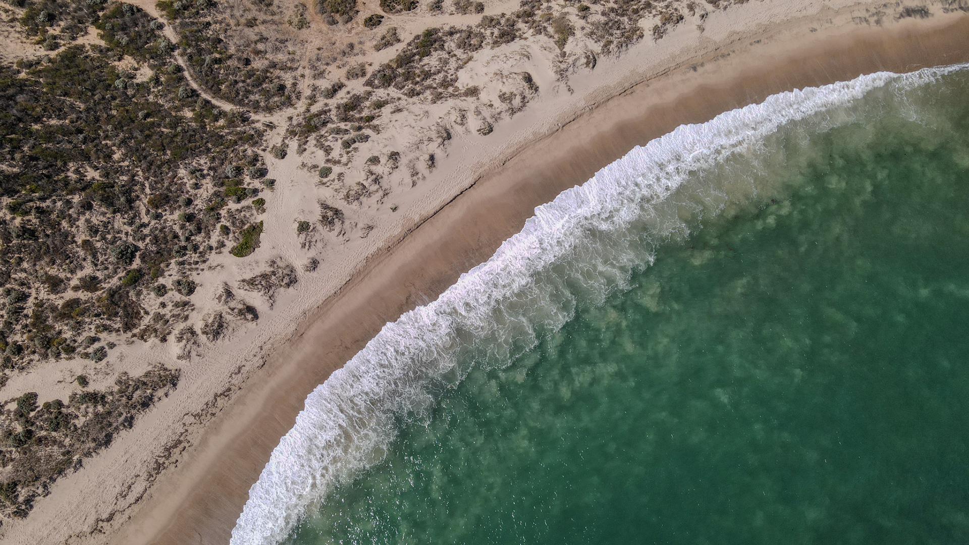 An aerial view showcases serene waves breaking on a sandy beach, highlighting nature's beauty and the peaceful coastline.
