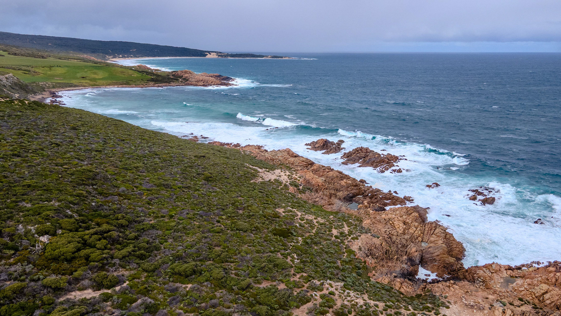 A breathtaking aerial view of a rugged coastal landscape showcasing dramatic rocky outcrops and lush greenery meeting the vibrant blue ocean waves. The scene captures the untouched natural beauty of the coastline, with waves breaking against the rocks and the horizon stretching into the distance. Ideal for travel, nature, or environmental projects.