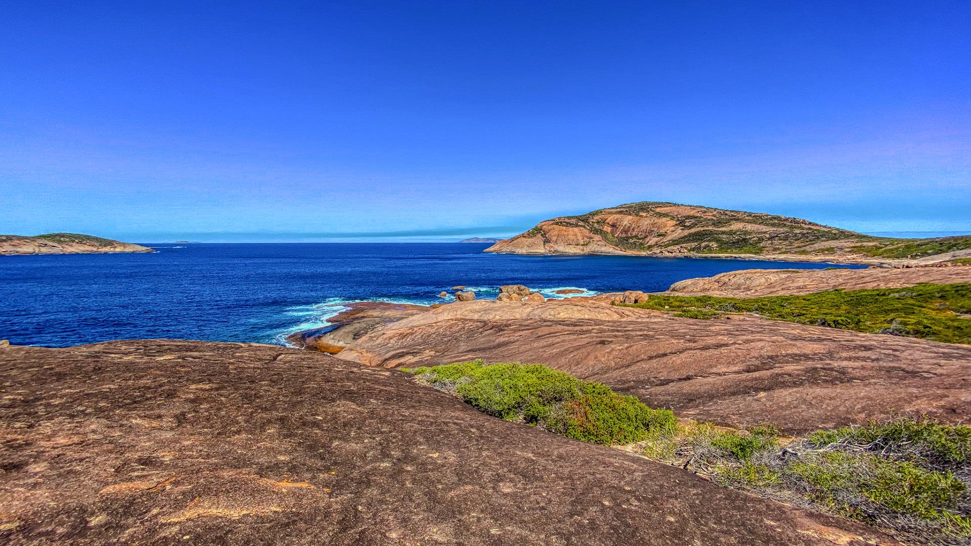 A tranquil coastal scene features a deep blue ocean, rocky coastline, and bright blue sky. Natural beauty and serenity abound.