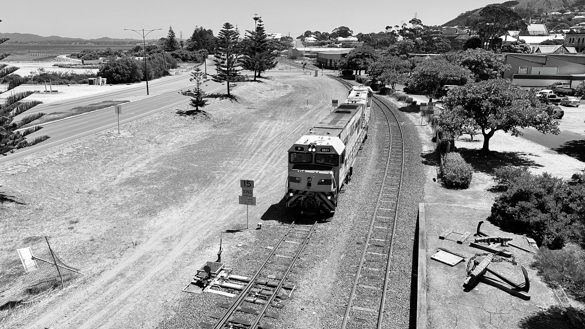 This black and white aerial view shows a train moving along a curved track through a semi-arid landscape, connecting communities.