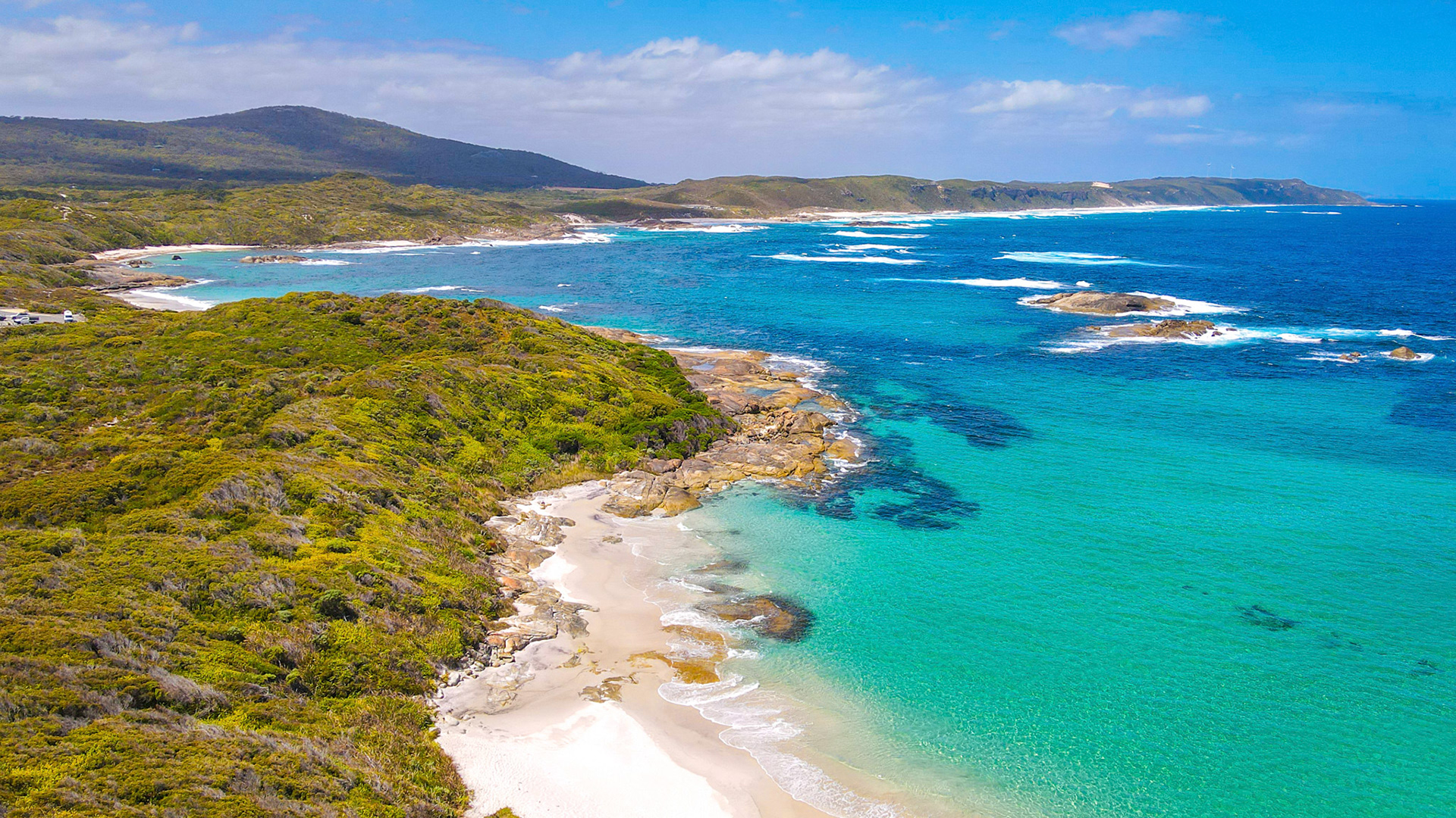 Experience the serene beauty of a rugged coastline, where lush vegetation meets the vibrant ocean waves and sandy beaches.