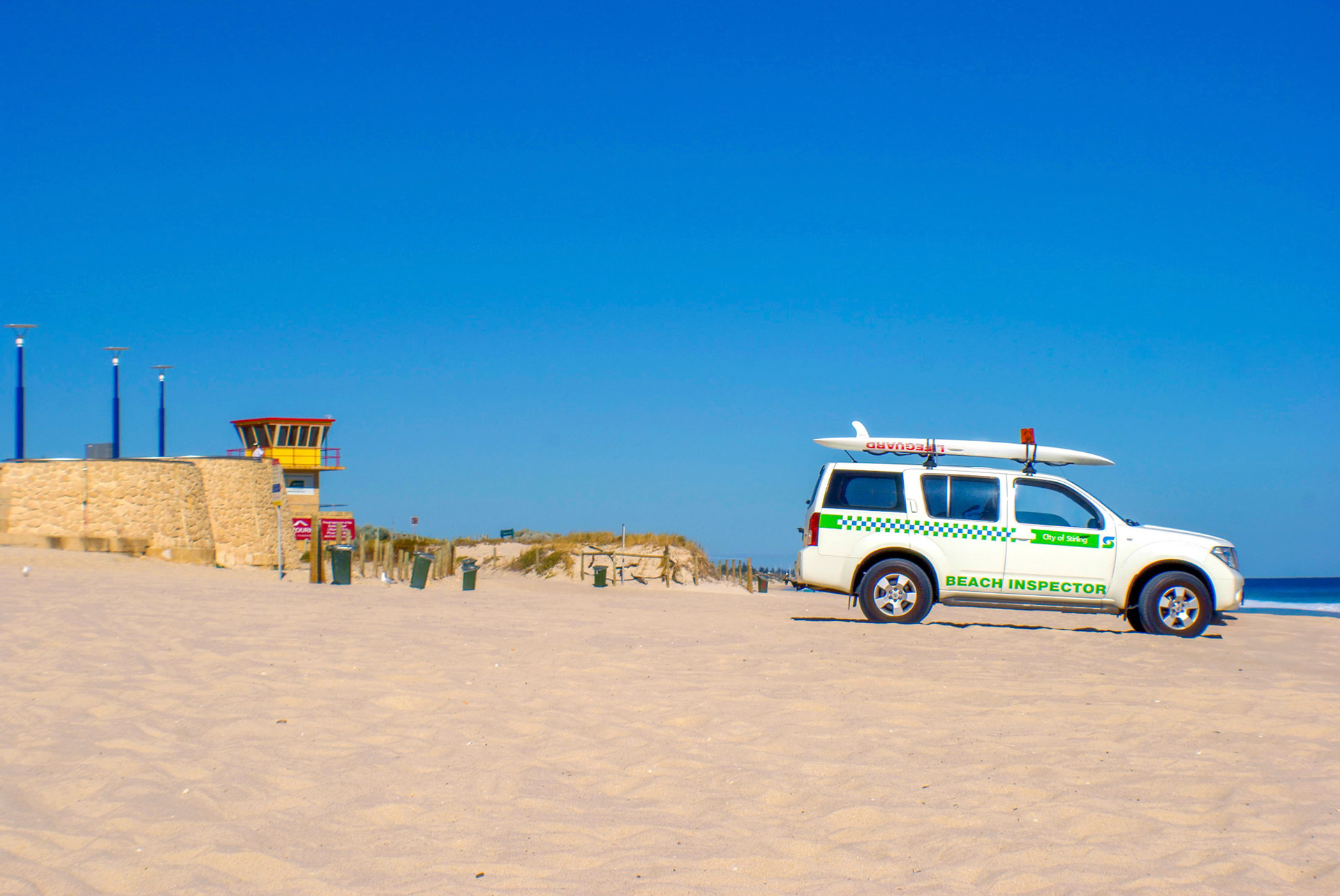 A beach inspector vehicle with a surfboard is parked on a sandy beach, ensuring safety and readiness for coastal activities.