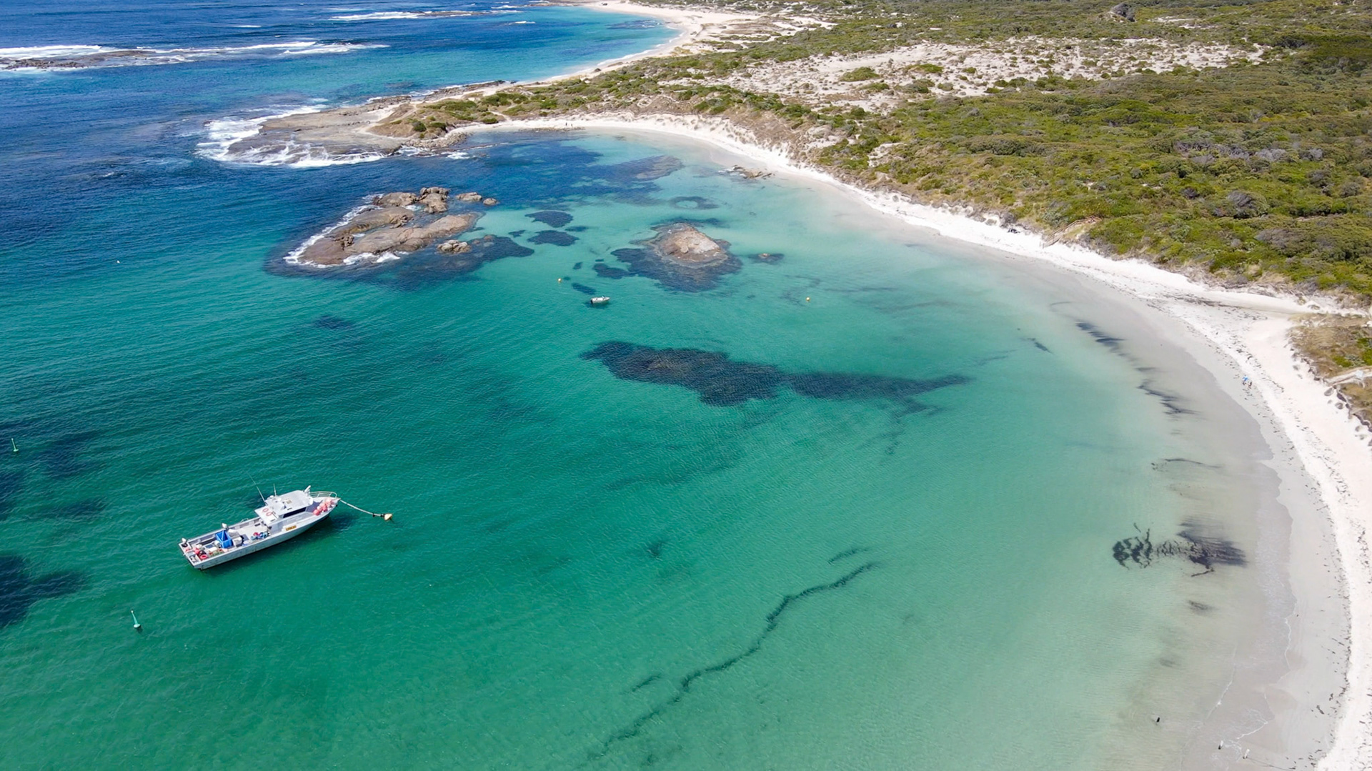 This serene coastal landscape features a boat anchored in turquoise waters, bordered by lush vegetation and a sandy beach.