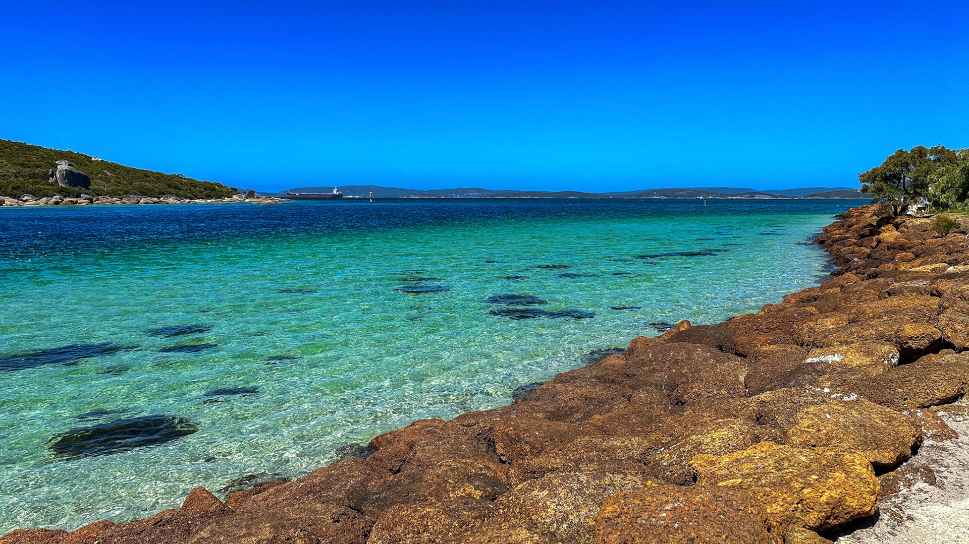 A panoramic view showcases a tranquil ocean meeting a rocky coastline under a vibrant sky. The serene landscape invites relaxation.