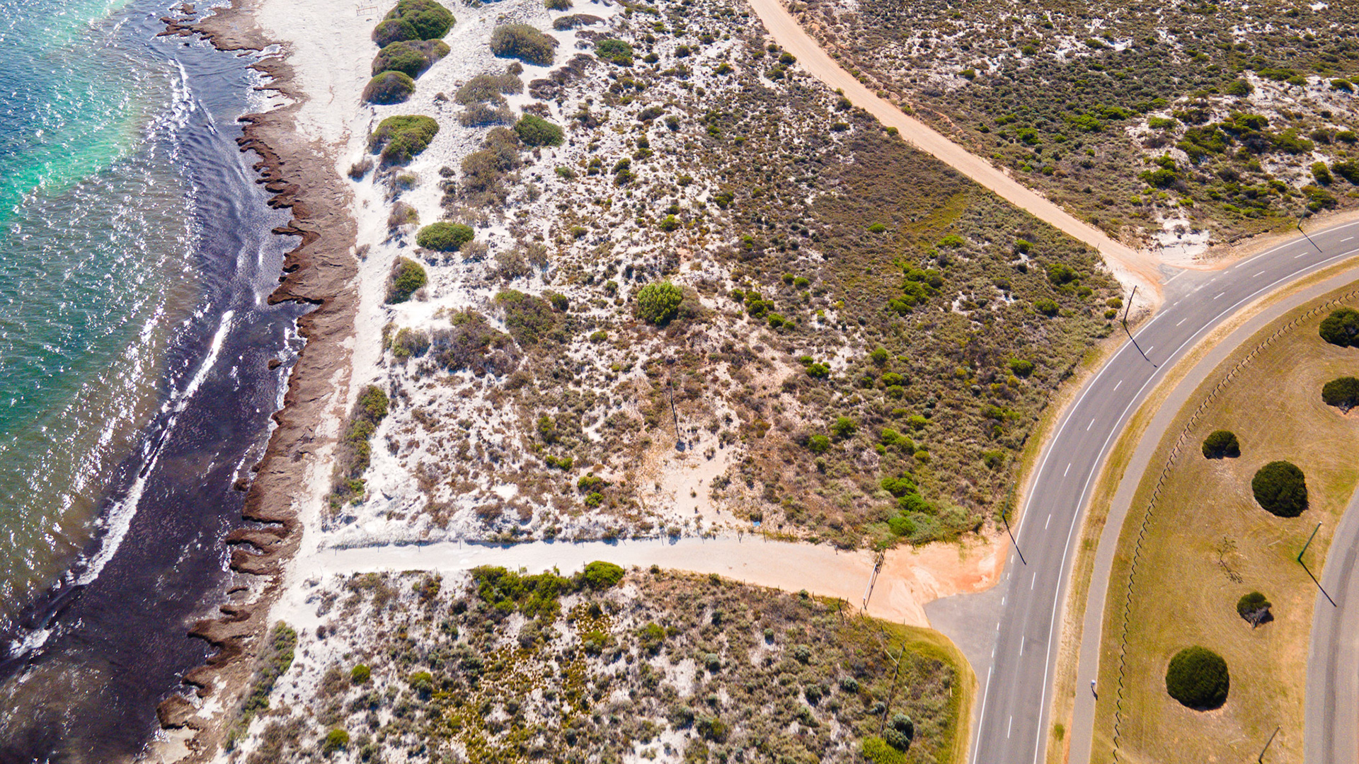Explore a serene coastal landscape where a road winds through nature, connecting the ocean and shore with stunning views.