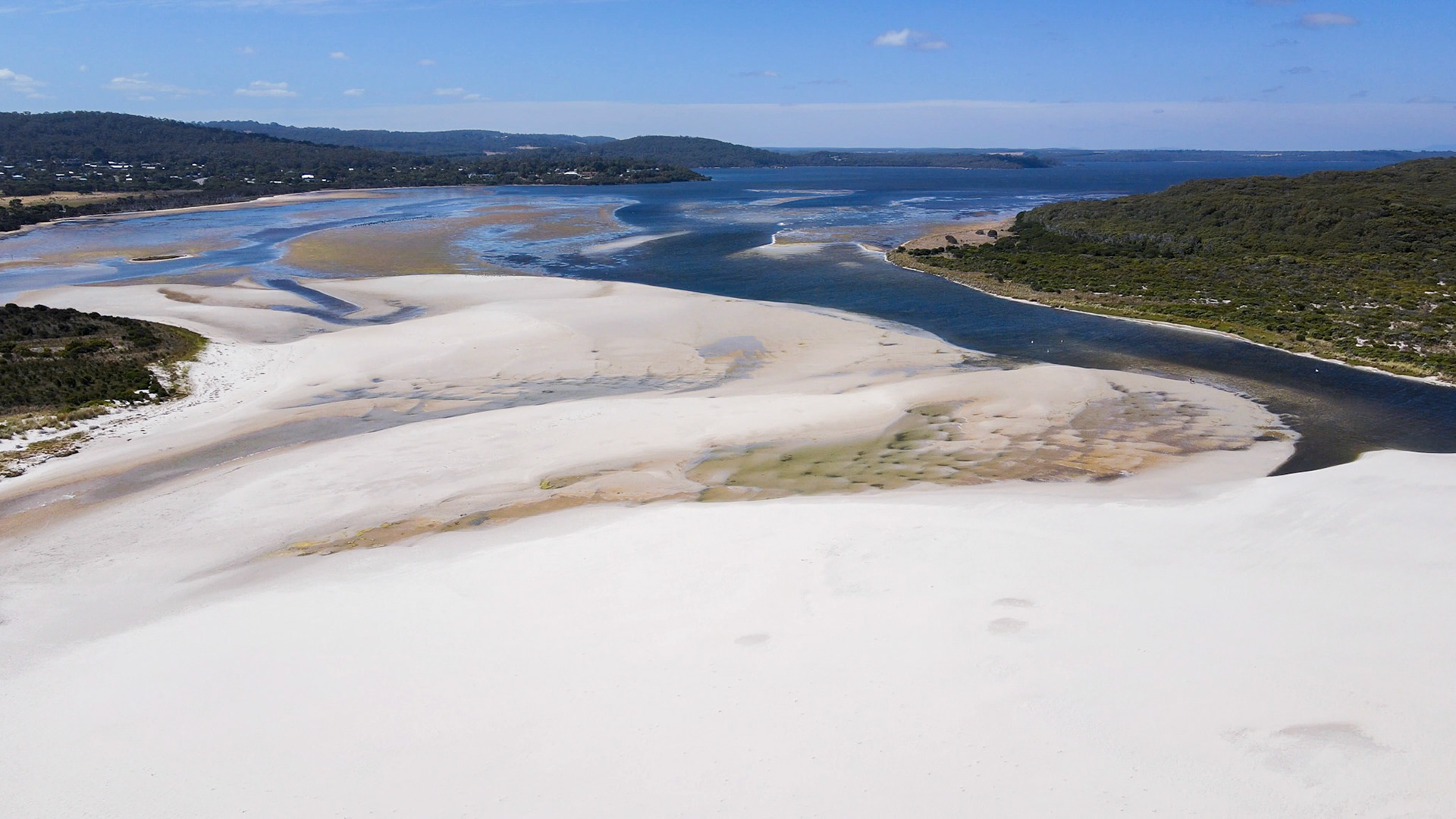 Experience the serene beauty of sand dunes meeting a tranquil river, showcasing nature's vastness and peaceful landscape.