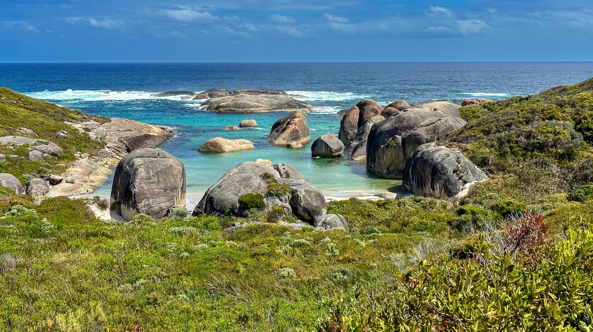 A serene coastal landscape features large boulders, turquoise ocean waters, and lush vegetation, evoking tranquility and natural beauty.