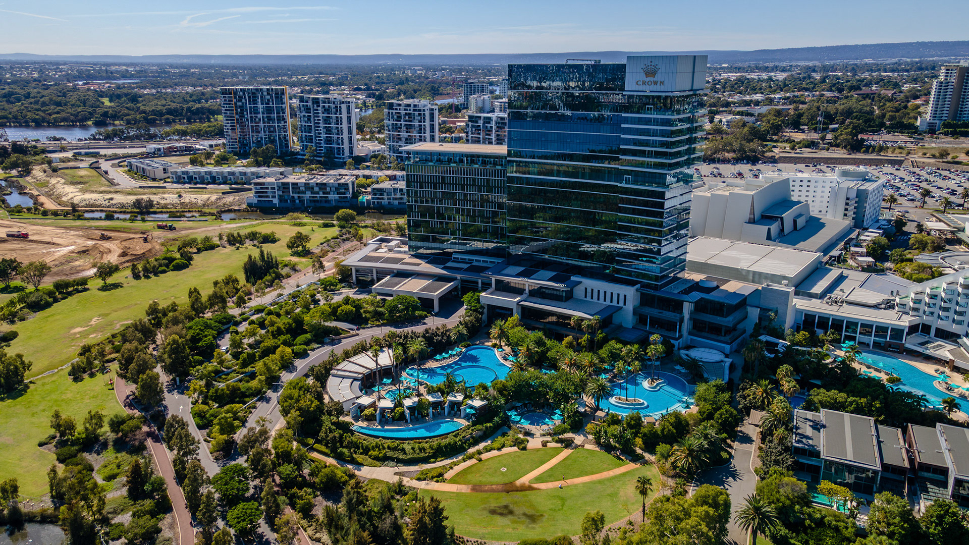 A breathtaking view captures a luxurious resort surrounded by lush greenery, sparkling pools, and modern buildings. The clear sky adds to the vibrant atmosphere, creating a perfect getaway setting.