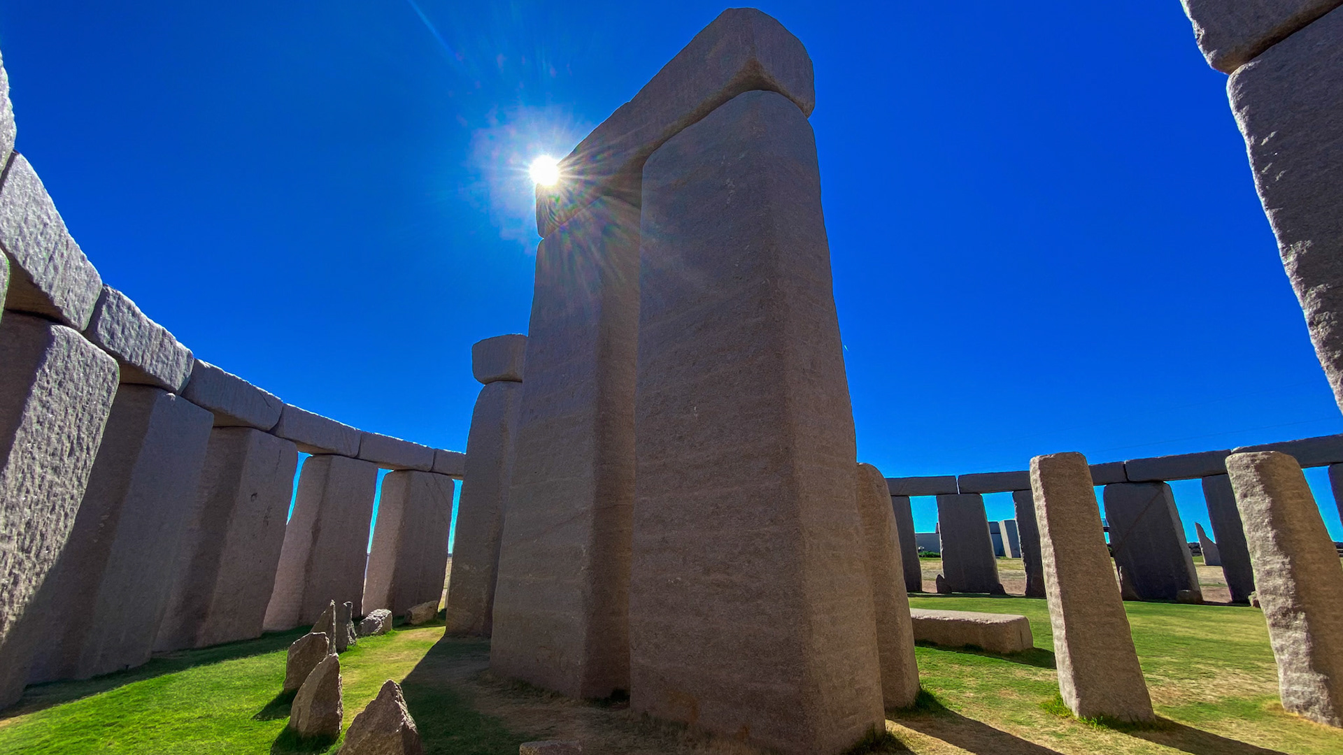 A wide-angle view of a Stonehenge replica showcases its ancient stones under a sunny sky, highlighting its historical significance.