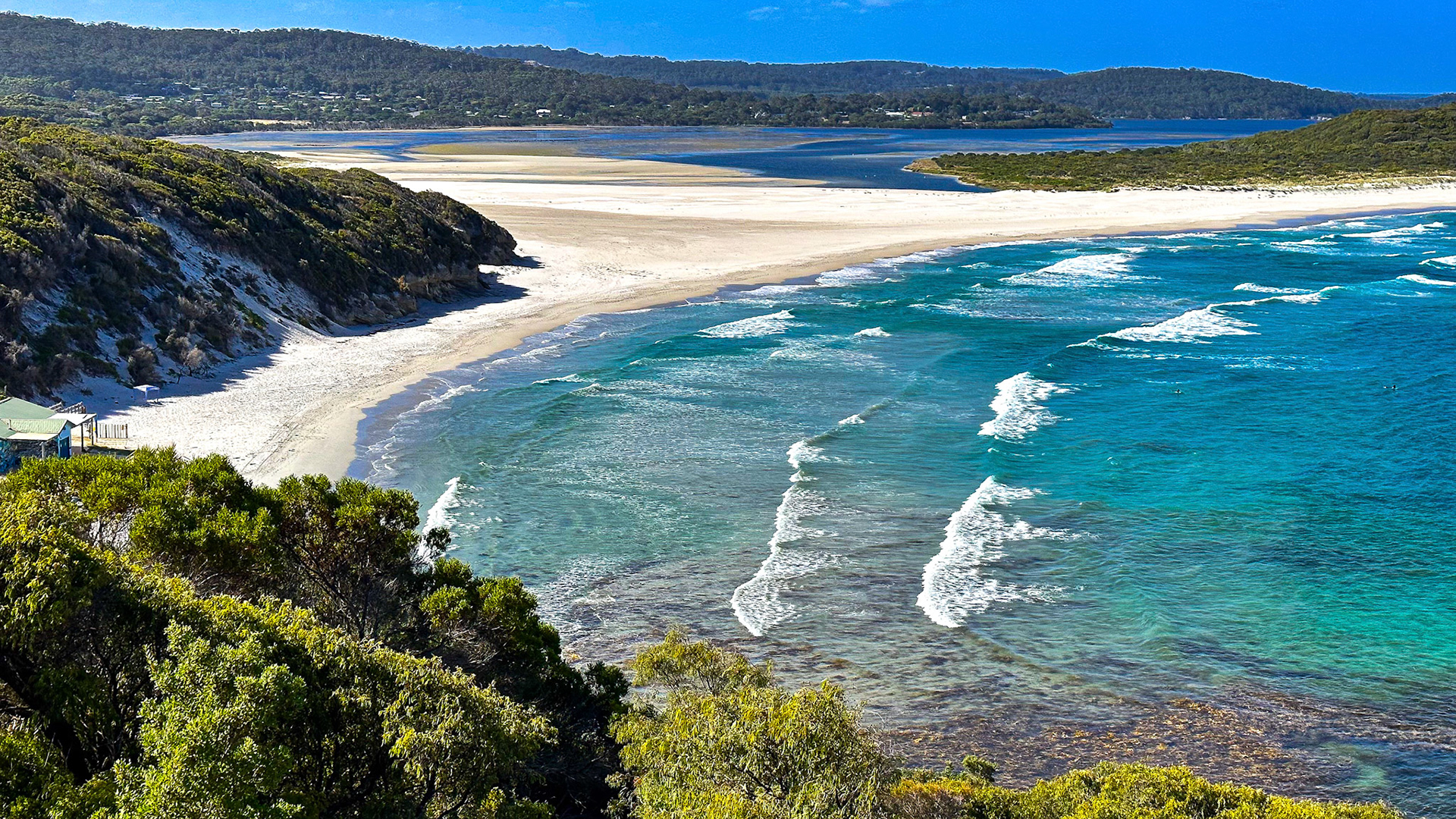 A panoramic view showcases a serene beach with turquoise waters, sandy dunes, and vibrant foliage, evoking tranquility and natural beauty.