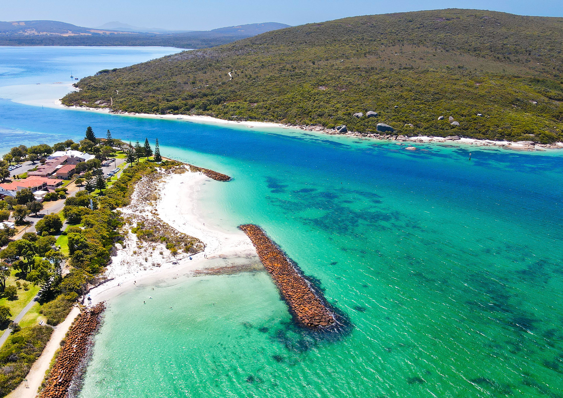 Experience the serene beauty of a coastal town, nestled by the bay, with vibrant waters and lush hills, perfect for relaxation.