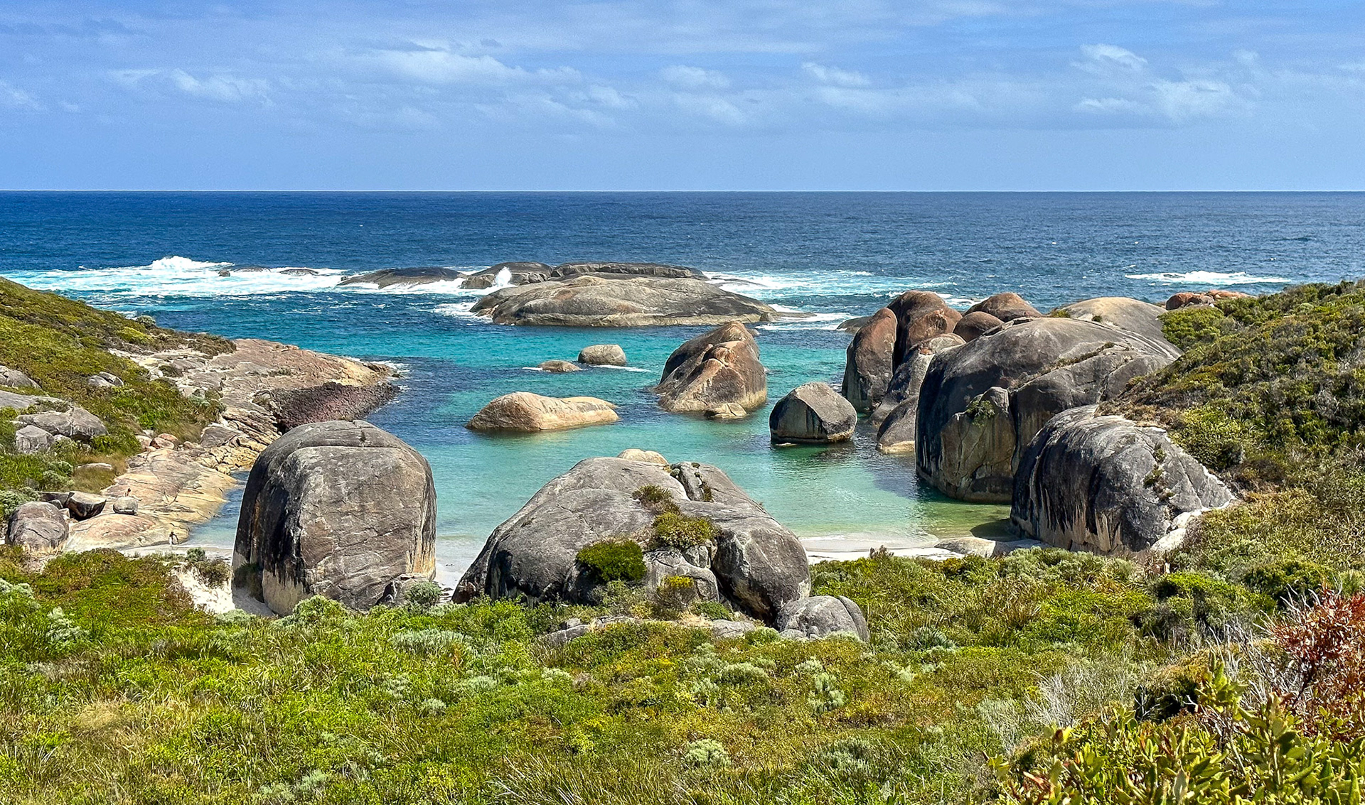 A serene coastal landscape features weathered boulders, turquoise water, and lush vegetation, evoking tranquility and natural beauty.