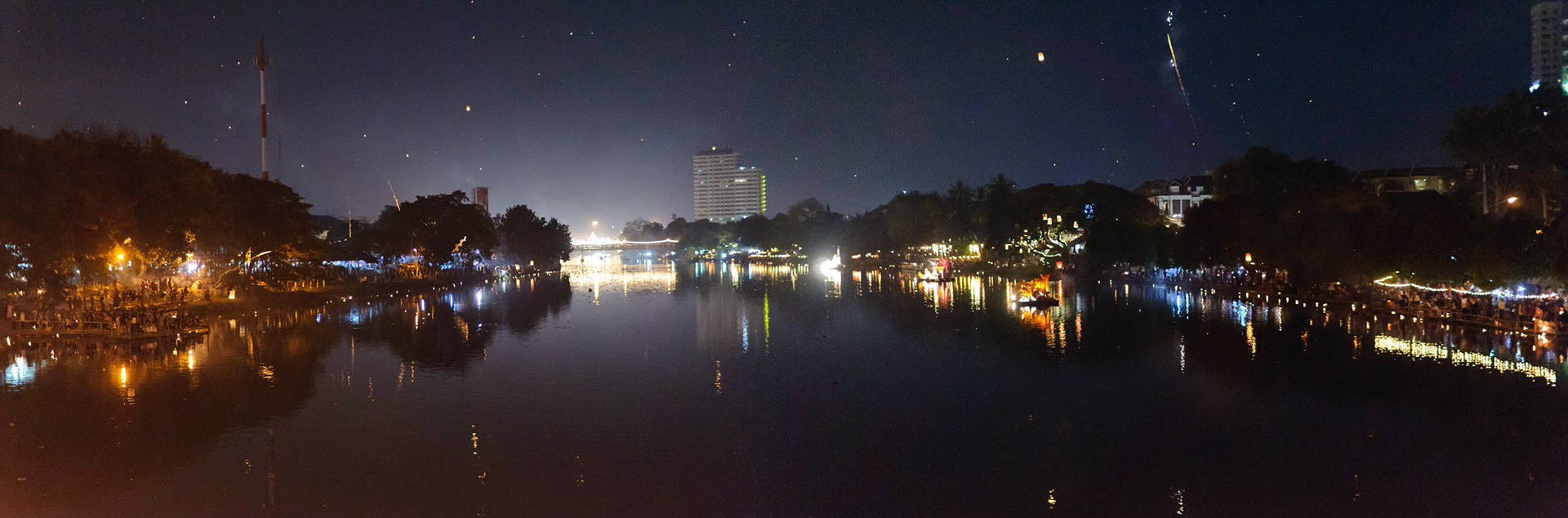 Krathongs being paced in river the along the banks, giant illuminated krathongs displays moored at the sides, fireworks being lunched from each bank and sky lanterns drifting through the sky.