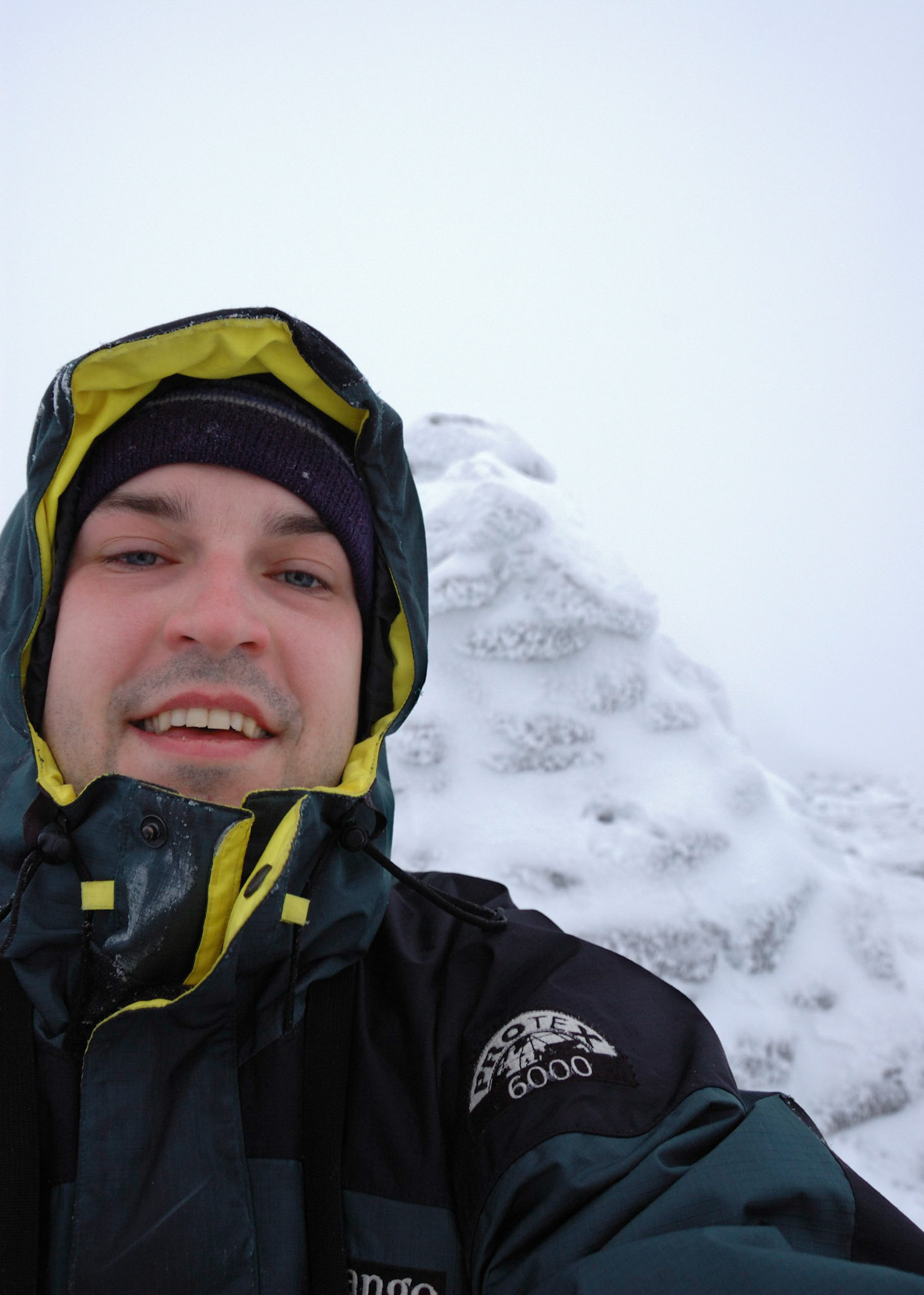 The summit of Cairn Gorm: sheltering behind the cairn, forcing a smile, rapidly losing any sense of feeling to the incredibly cold wind.