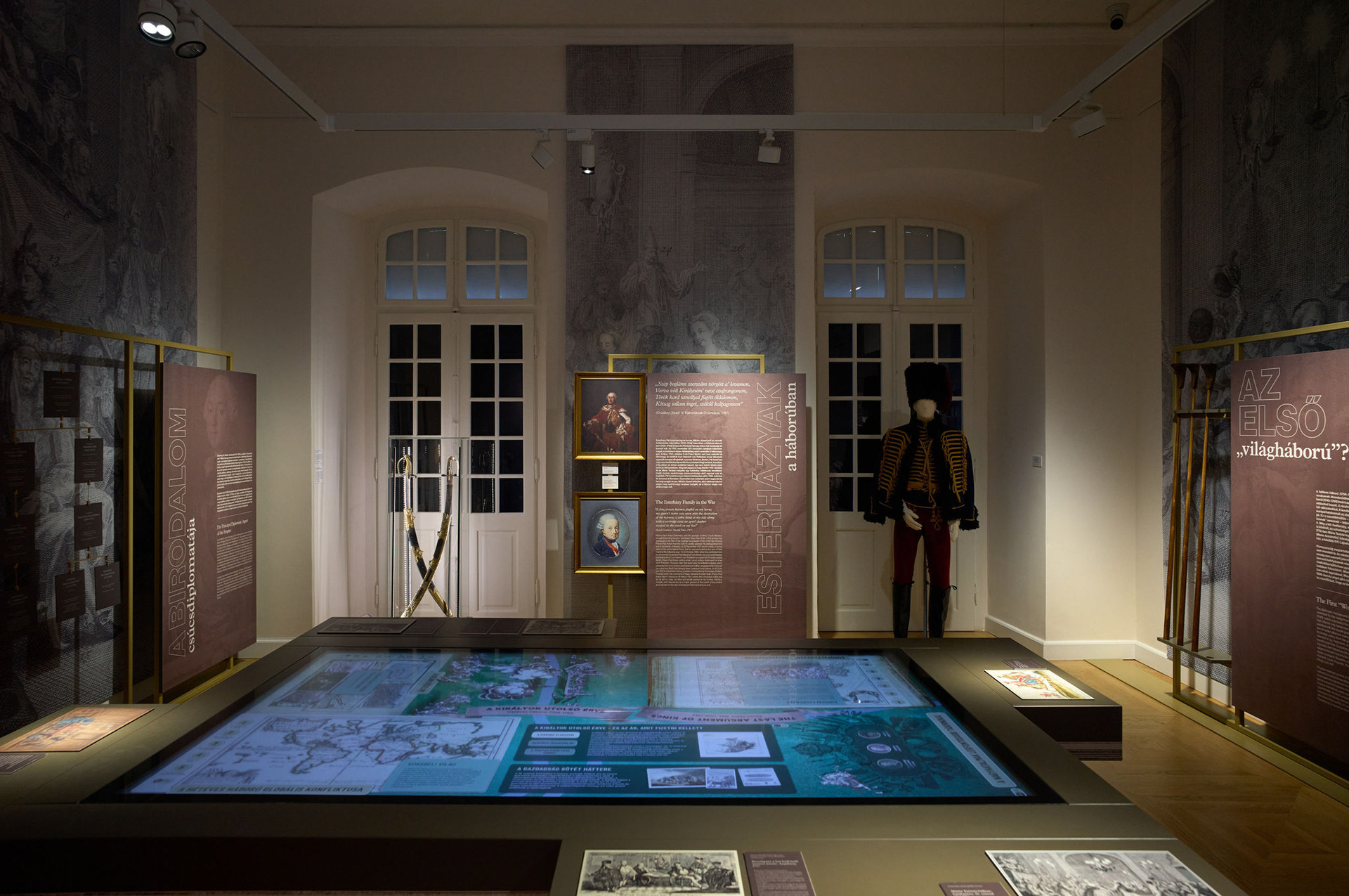 A kultúrateremtő katona kiállítás enteriőrje – interaktív asztal, történeti tárgyak és grafikai információs felületek