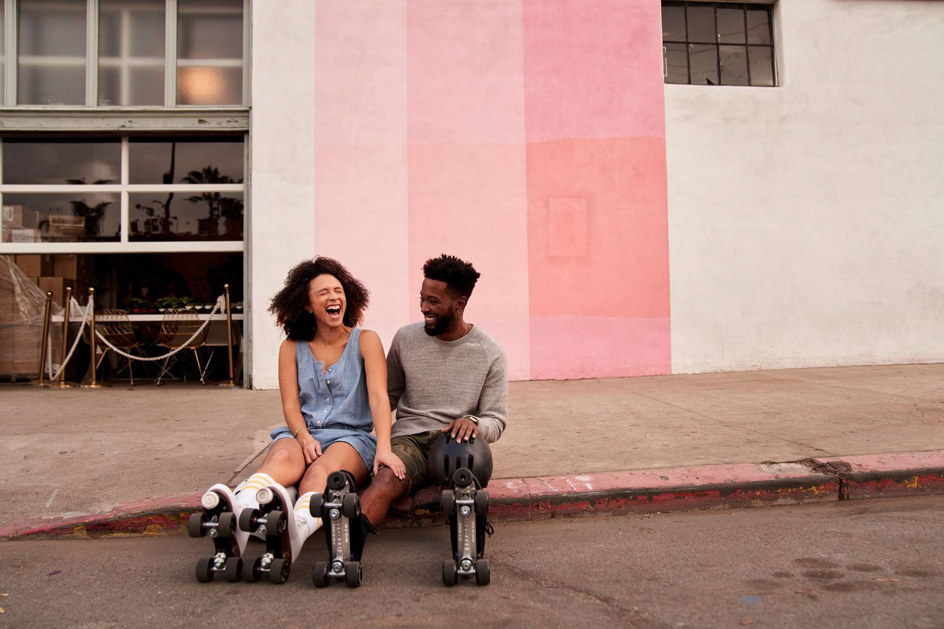 couple sitting on the sidewalk wearing rollerskates and laughing, BIPOC