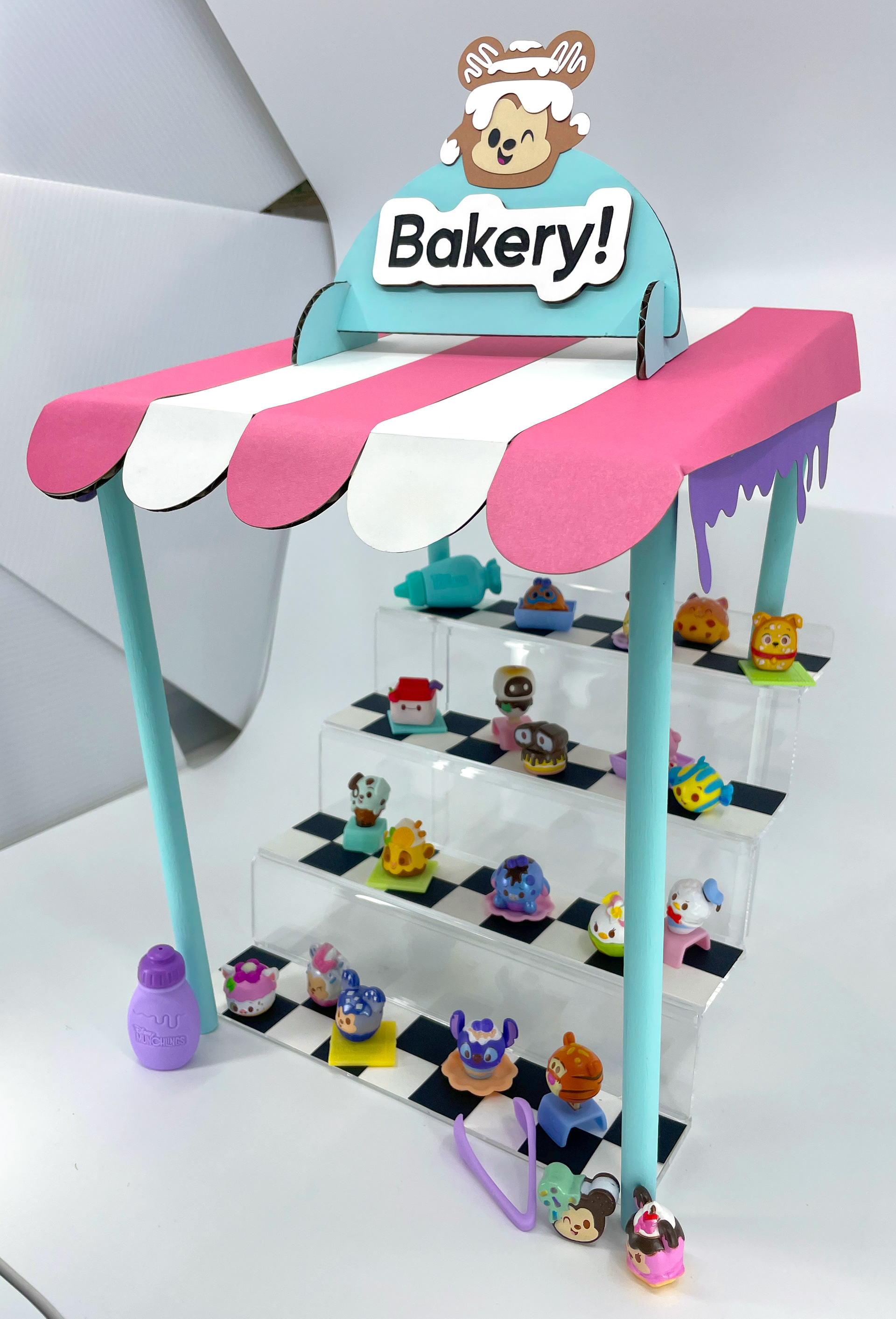 Disney Munchlings | Display Stand DIY: I created this original display stand for Disney Munchlings mini figures. I designed the folded cardboard awning, bakery sign, and decorative elements in Adobe Illustrator for use with my laser cutter. The final touches were hand-painted.  Click "view" to see the final video on TikTok.  I acted as "the hands" in the final video, which is currently the top-performing video on TikTok for Disney Munchlings.