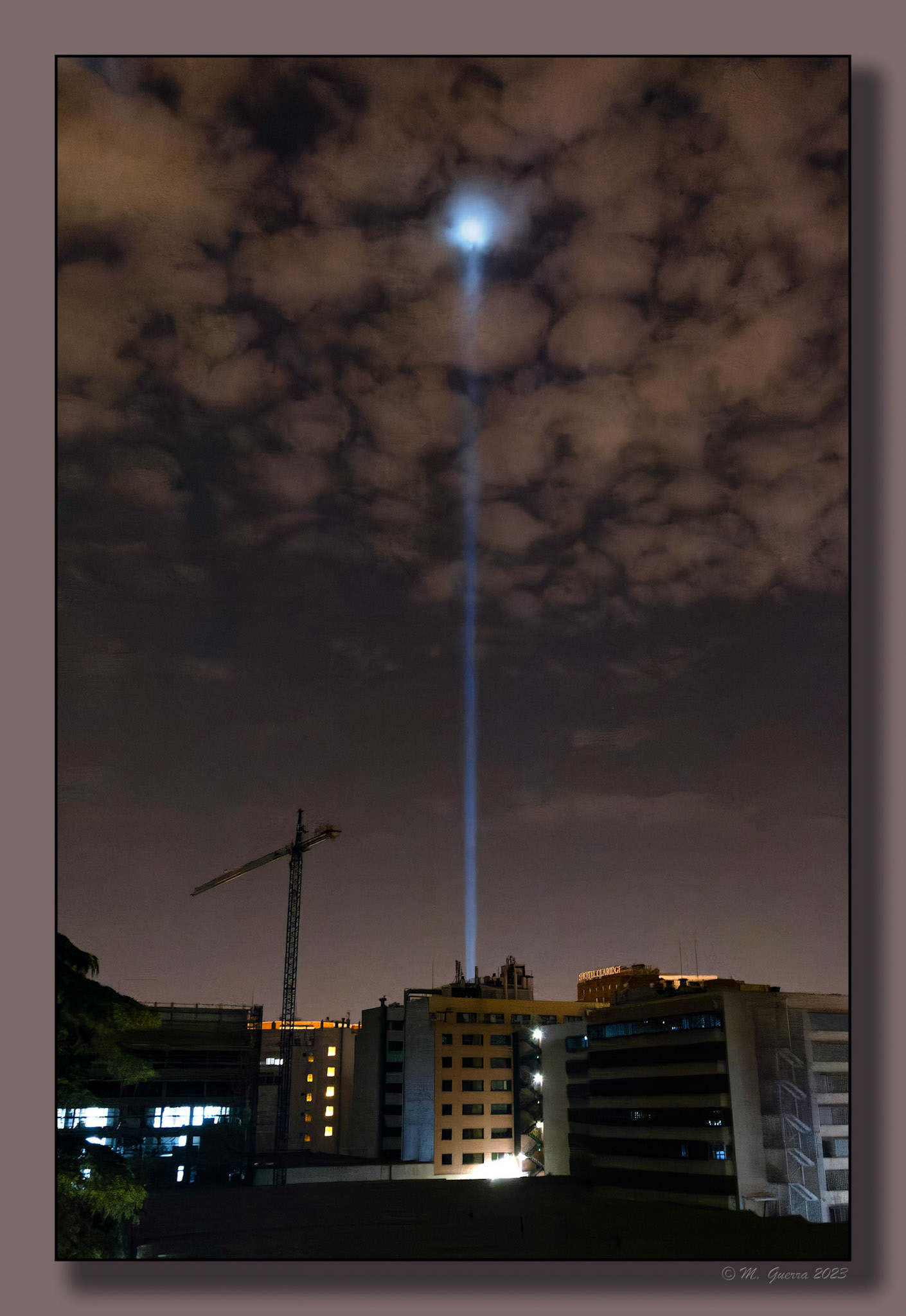 Rayo láser apuntando al cielo e impactando en unas nubes sobre Madrid de noche