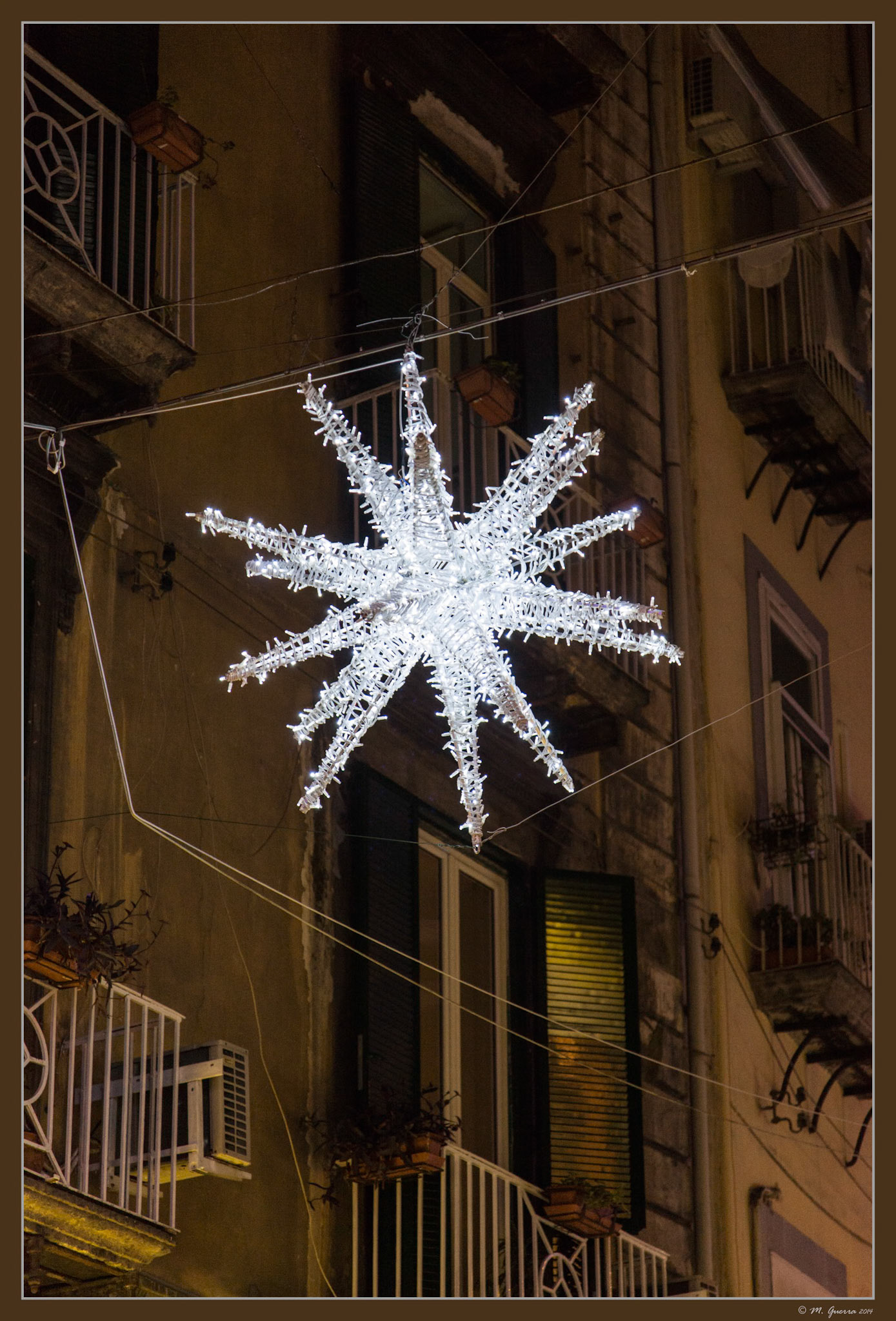 Bola gigante de Navidad colgada e iluminada en una calle de Nápoles. Ampliar