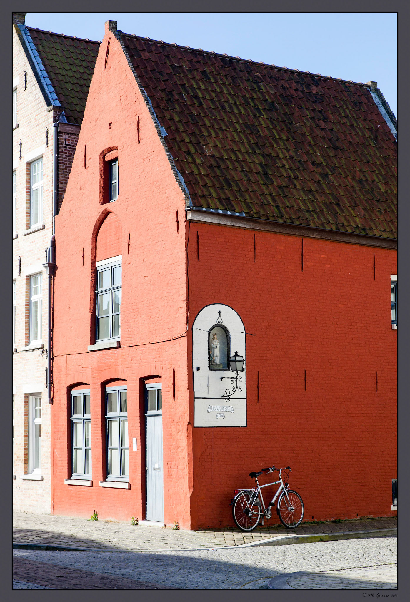 Bici aparcada al lado de una casa roja en Brujas. Ampliar