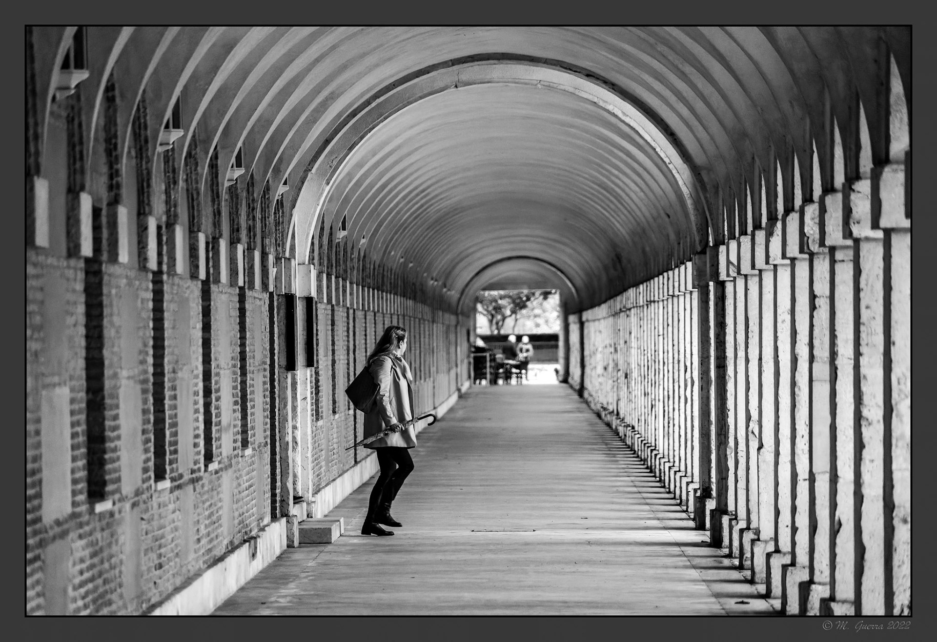 Pasillo cubierto con arcos en un anexo al Palacio Real de Aranjuez. Chica con paraguas. 100ASA