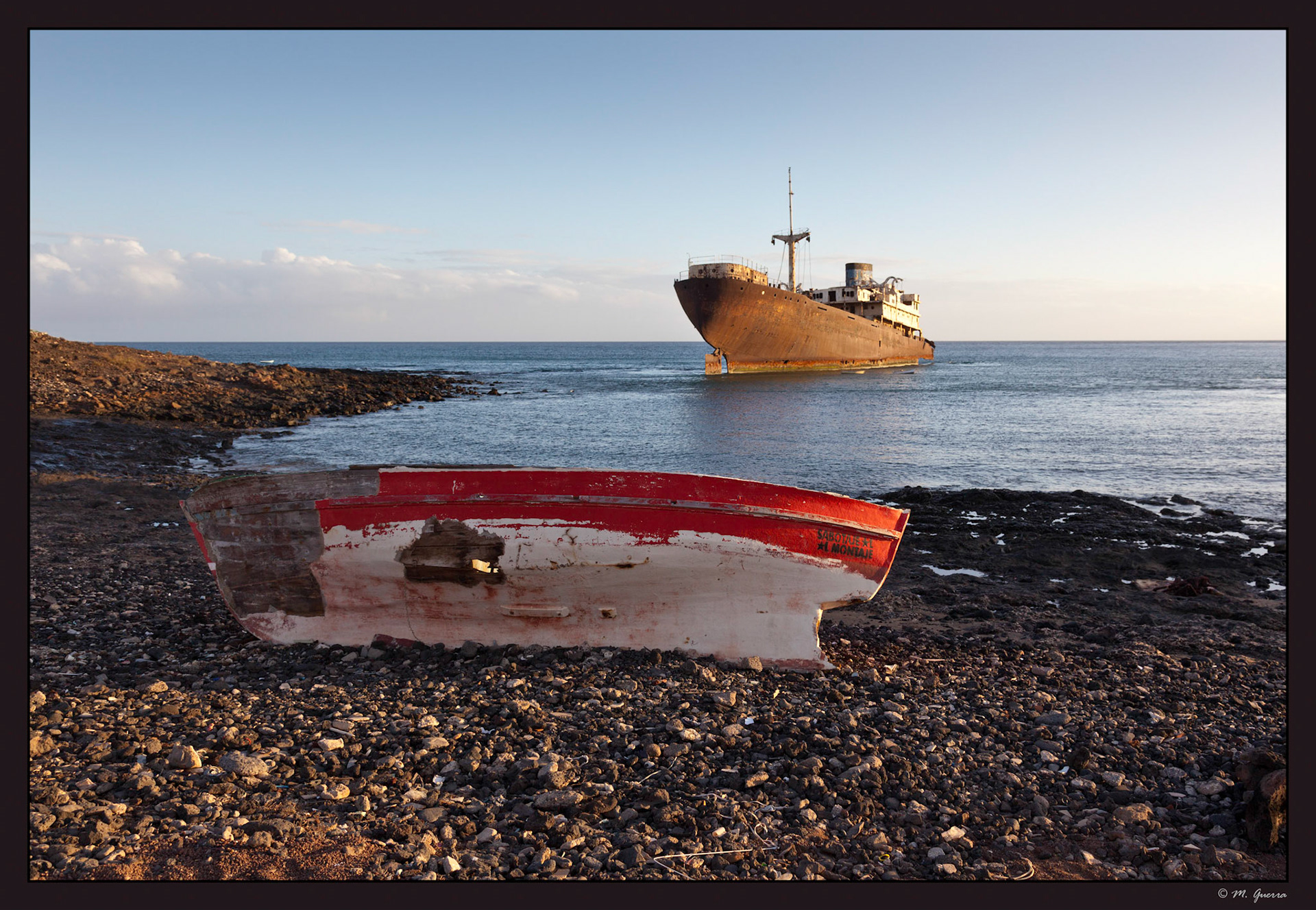 El pecio de un barco medio hundido en Costa Teguise en Lanzarote con una barca destruida en primer plano. Ampliar