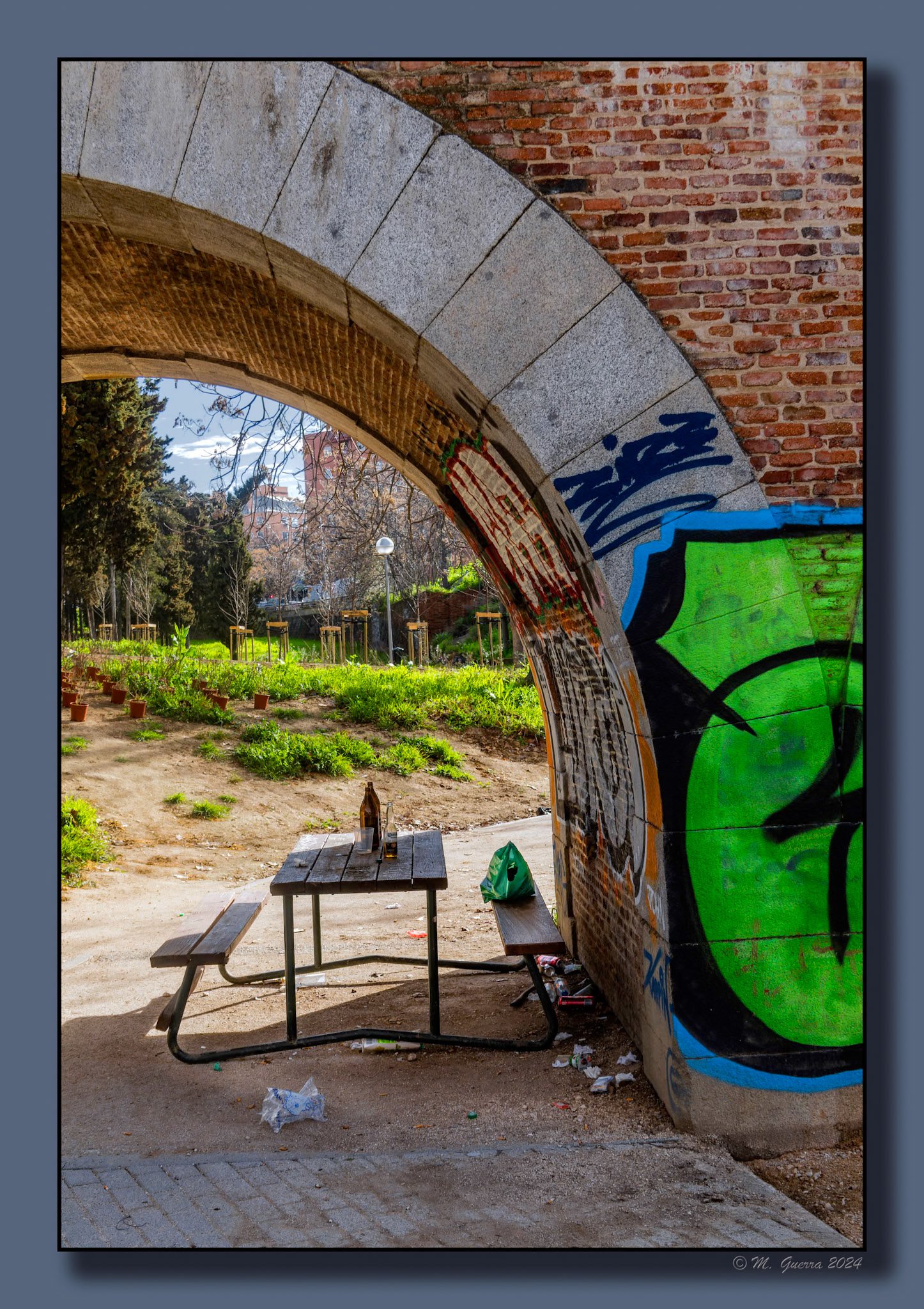 Mesa con botella y dos bancos bajo un antiguo viaducto del Canal de Isabel II en el parque de Agustín Rodríguez Sahagún