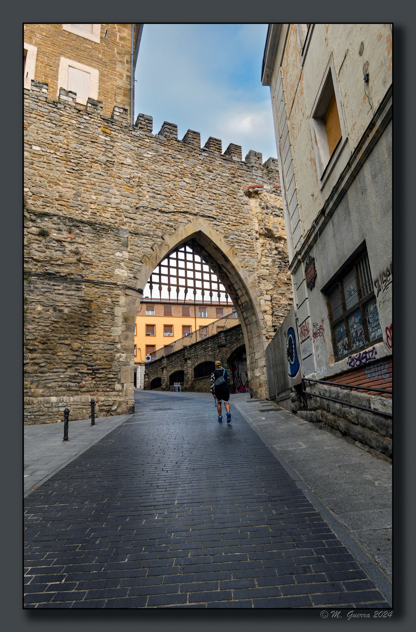 Calle en cuesta con arco final en Vitoria y un paseante