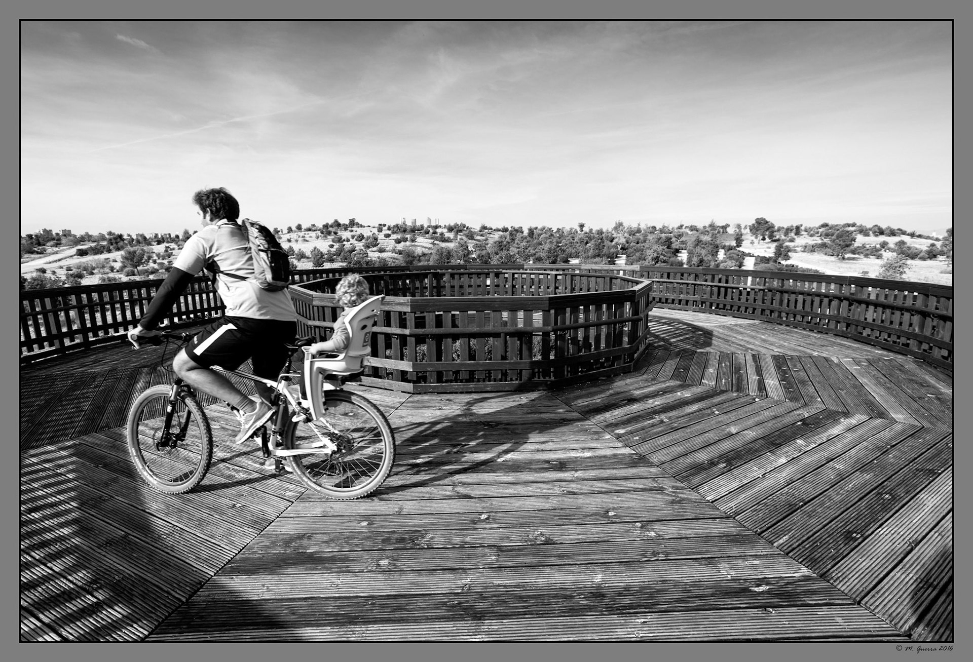 Un padre ciclista con su hijo en el Mirador circular de madera en El parque de Felipe VI. Ampliar