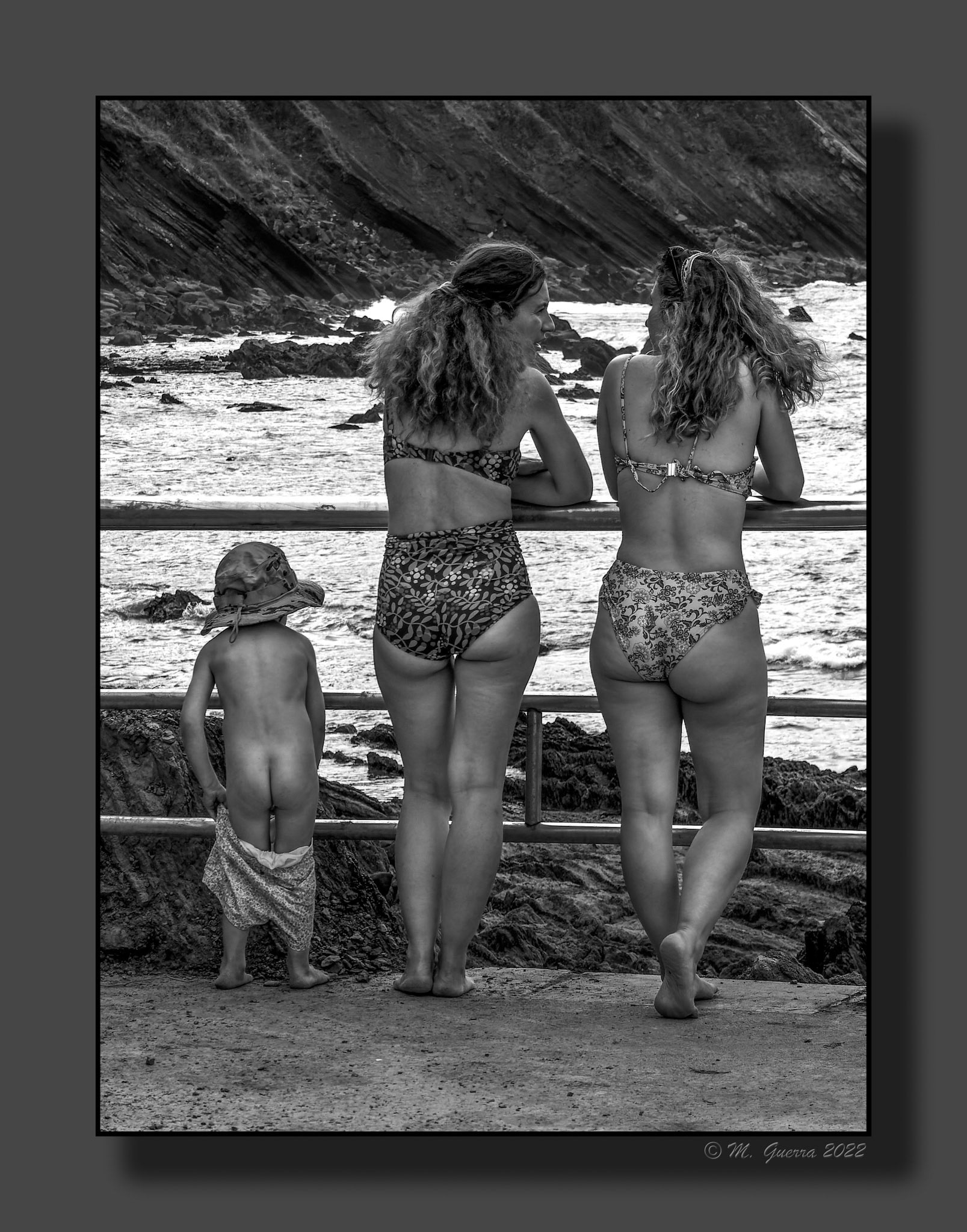 Dos chicas de espaldas y un niño desnudo en el paseo marítimo de Ribadesella. 100ASA