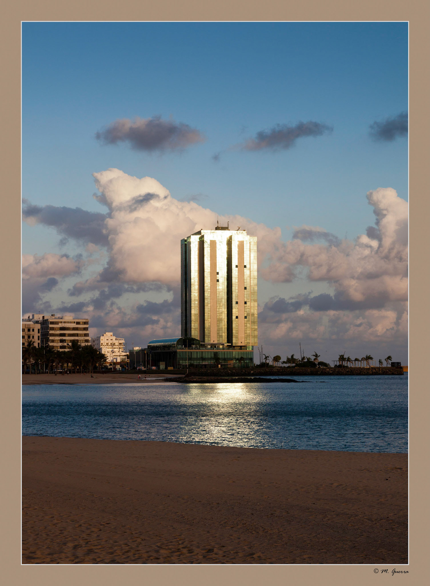 Edificio mamotreto, que rompe la imagen de Arrecife, reflejado al atardecer sobre el mar. Ampliar