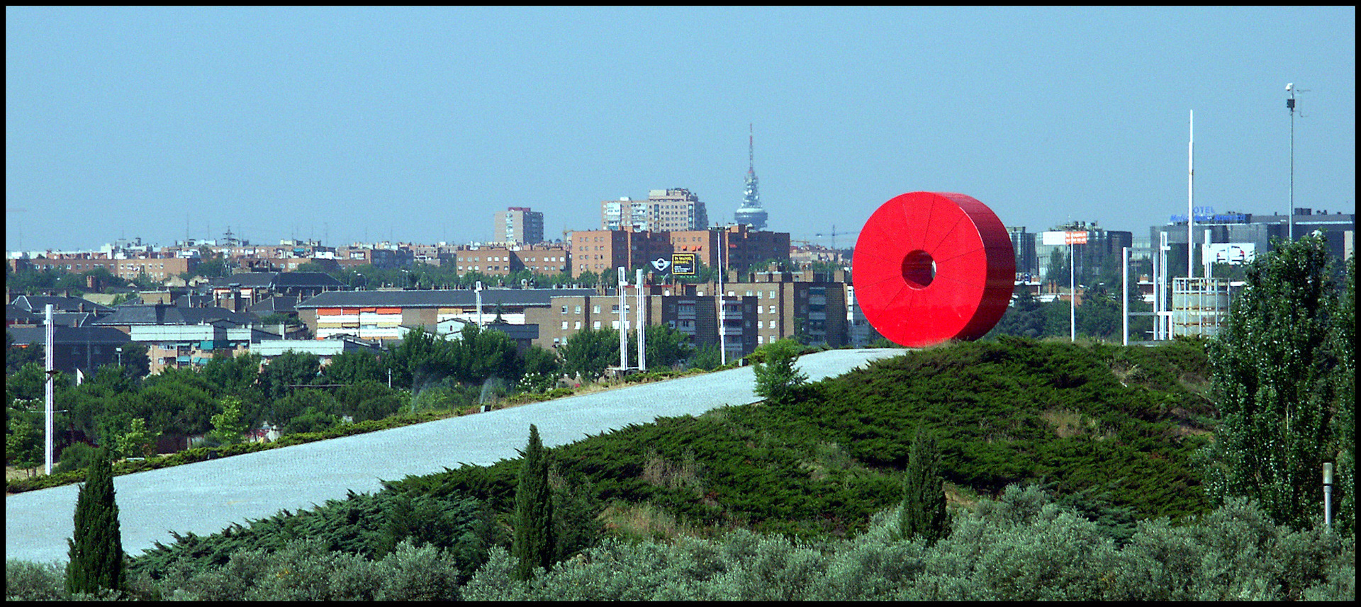 Una escultura de hierro rojo sobre las casas de Madrid en el parque de Juan Carlos I de Madrid. Ampliar