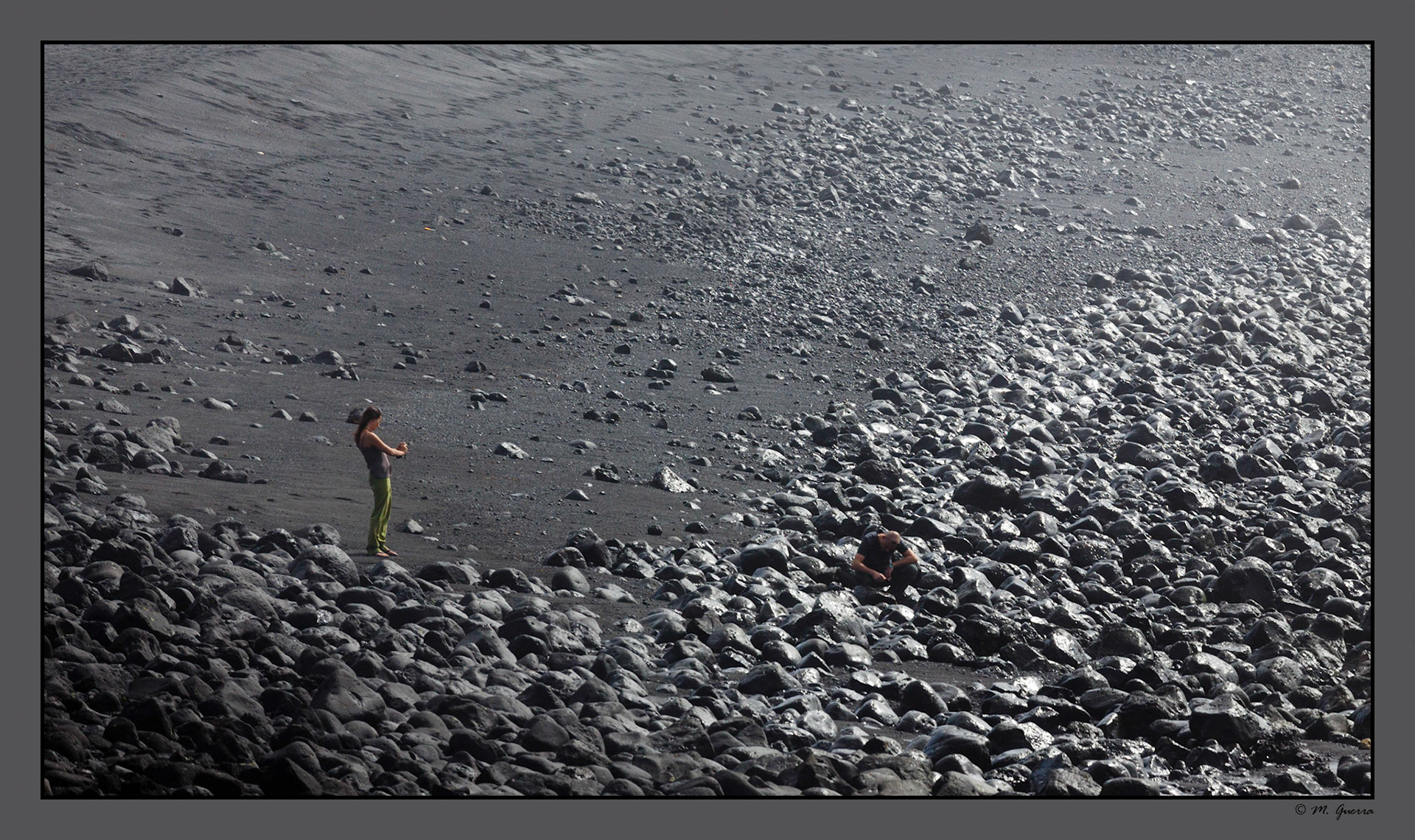 Una chica y un chico sentado en una playa rocosa en La costa entre Los Hervideros y las Salinas en Lanzarote. Ampliar