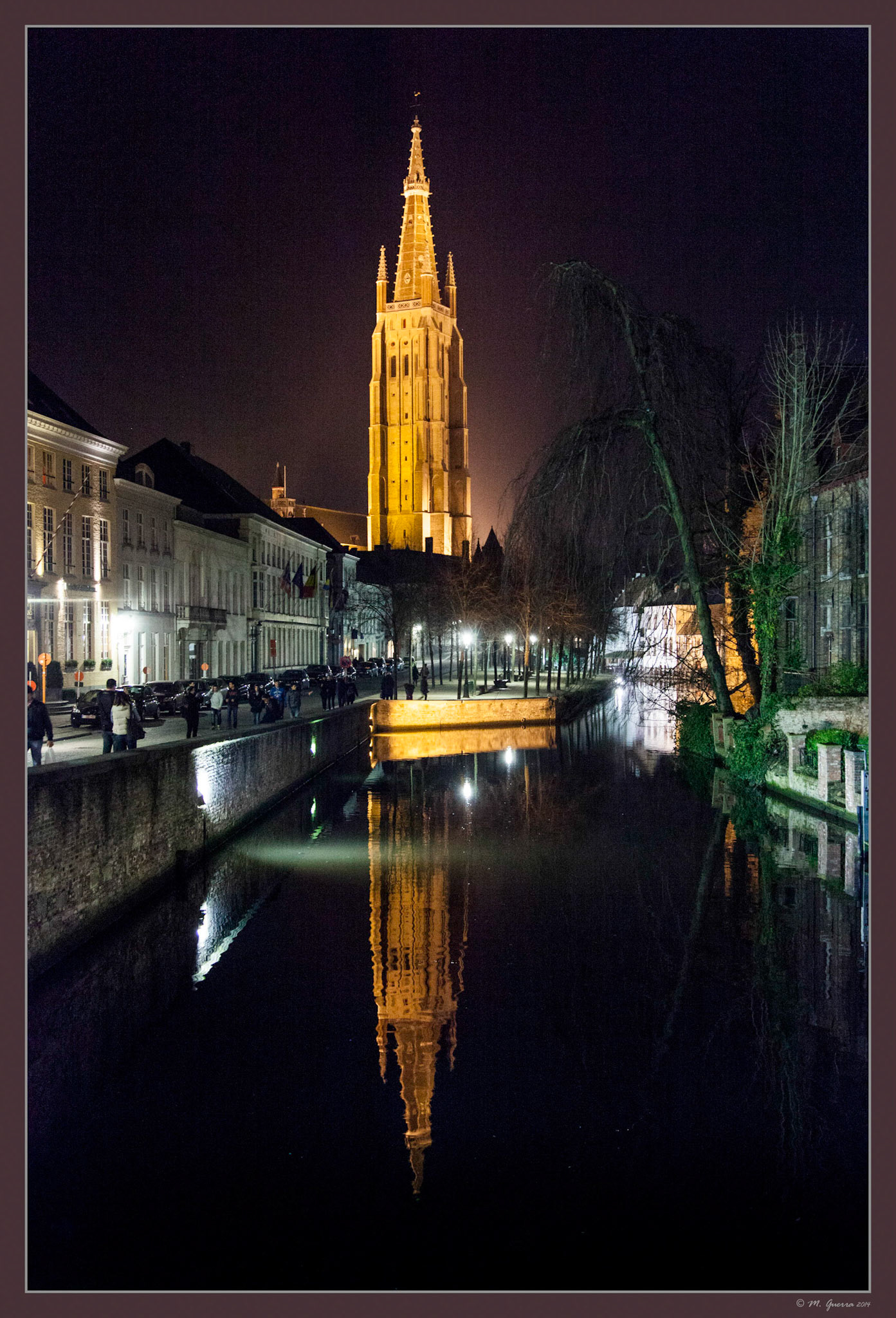 Torre iluminada en Brujas reflejada sobre un canal. Ampliar