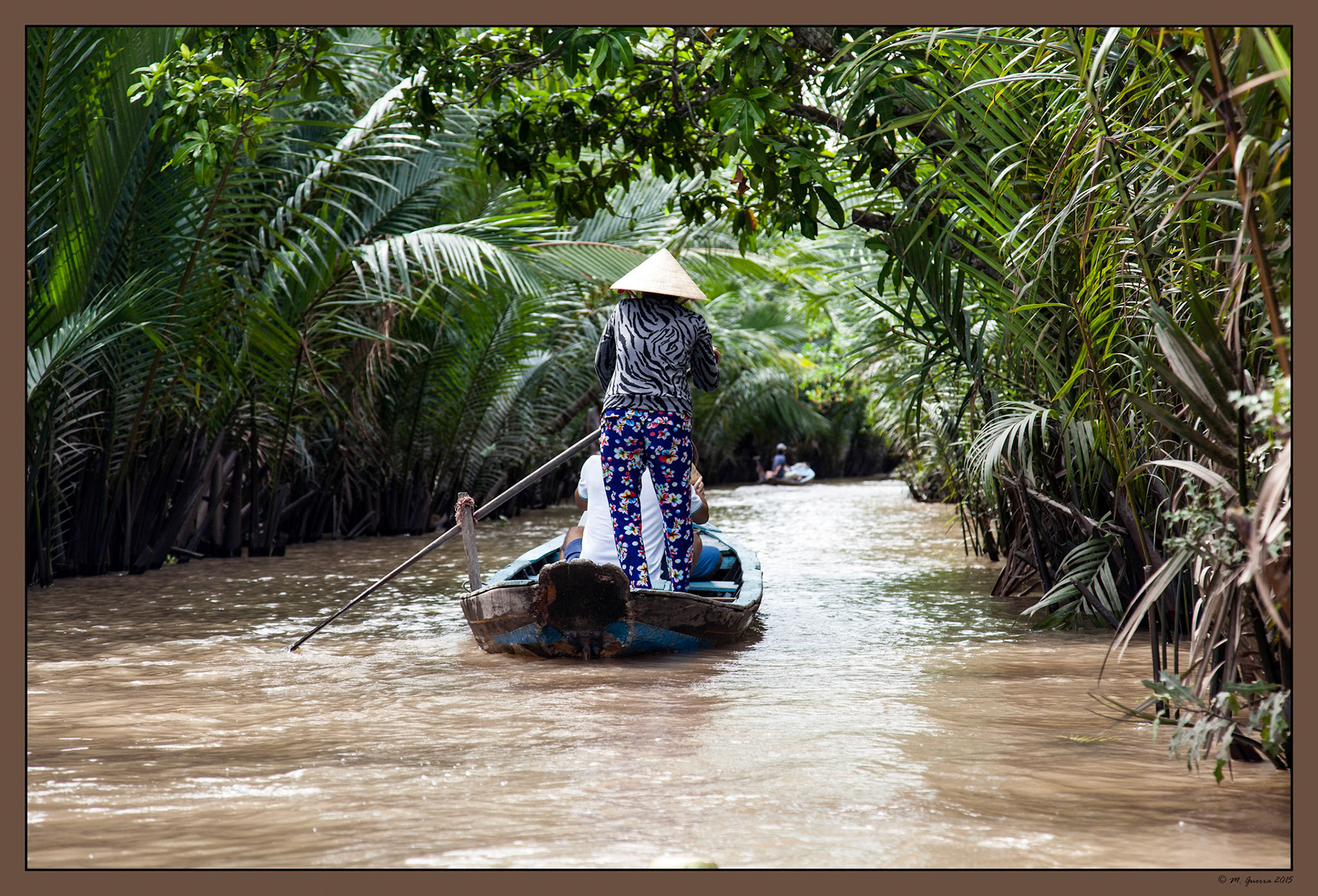 Barcaza para turistas en un canal rodeado de palmeras en el delta del Mekong. Ampliar