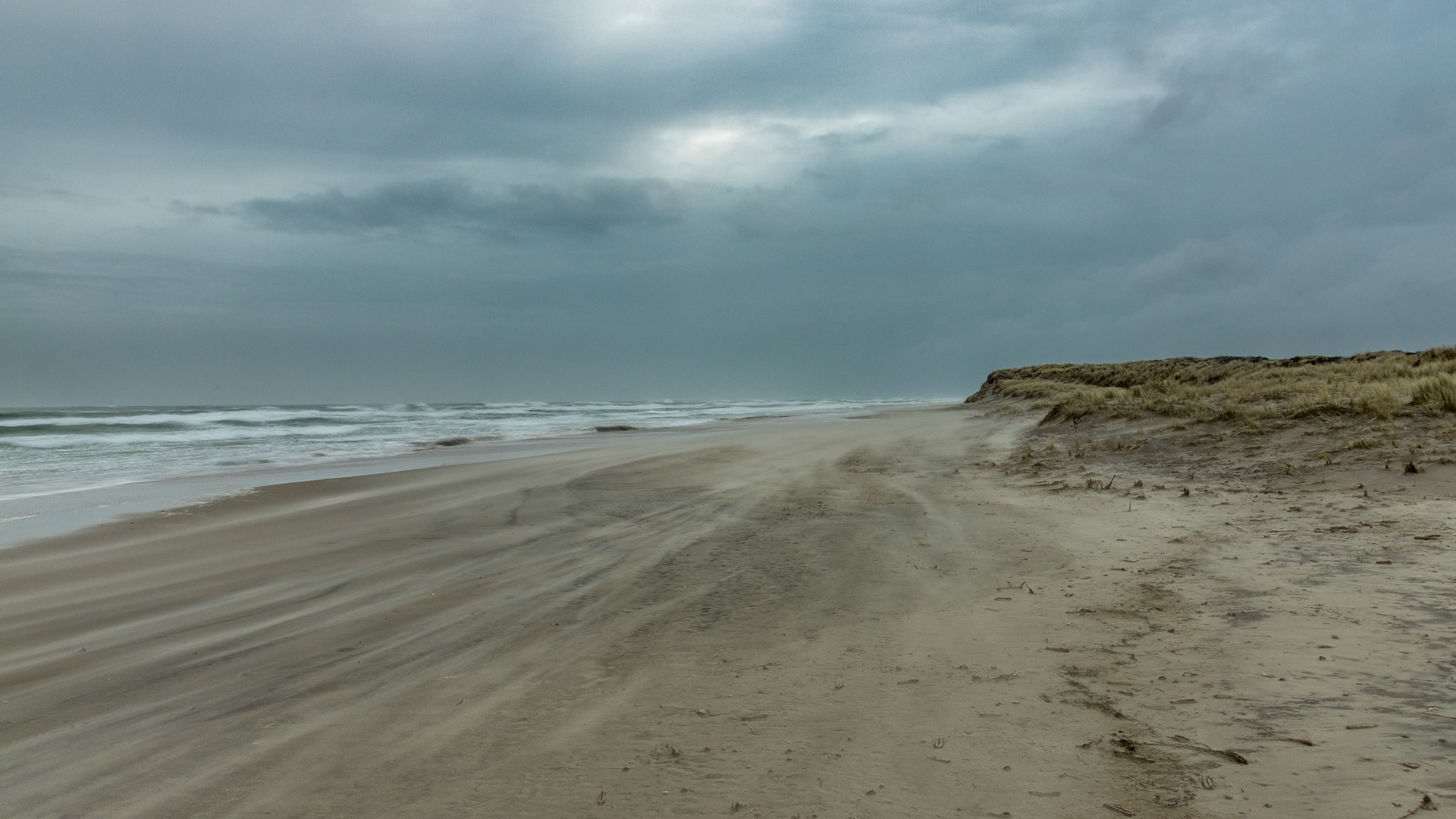 Het zand jaagt over het strand