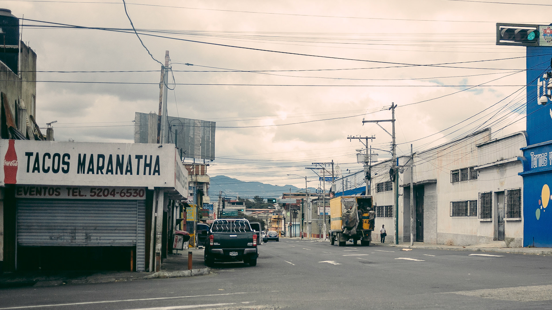 A rather uninteresting view of a Guatemala City intersection -- until you look closer. Yes, there is a man in a large bag hanging behind a box-truck-turned-trash-truck. Welcome to Guatemala.