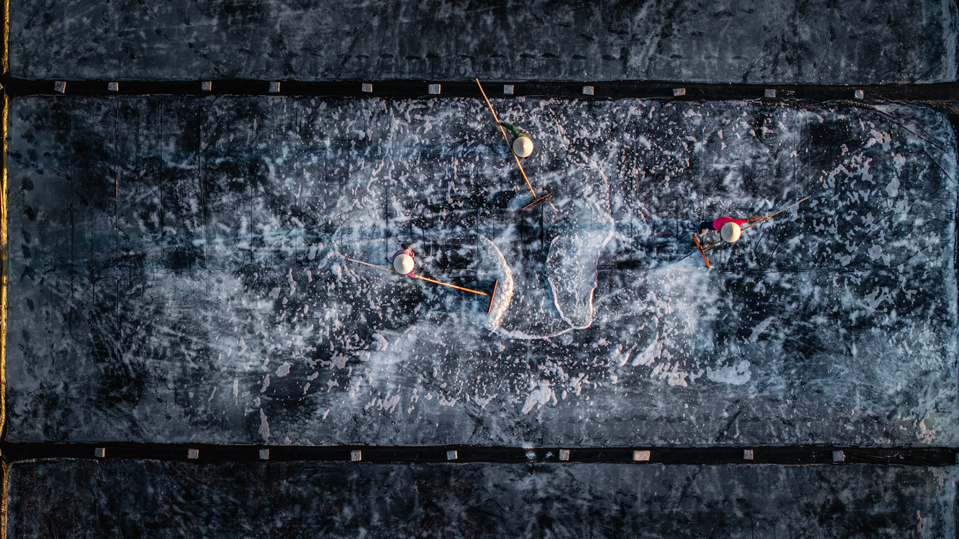 The evening harvest begins, transforming the industrial salt fields of Vietnam into a striking geometric canvas.