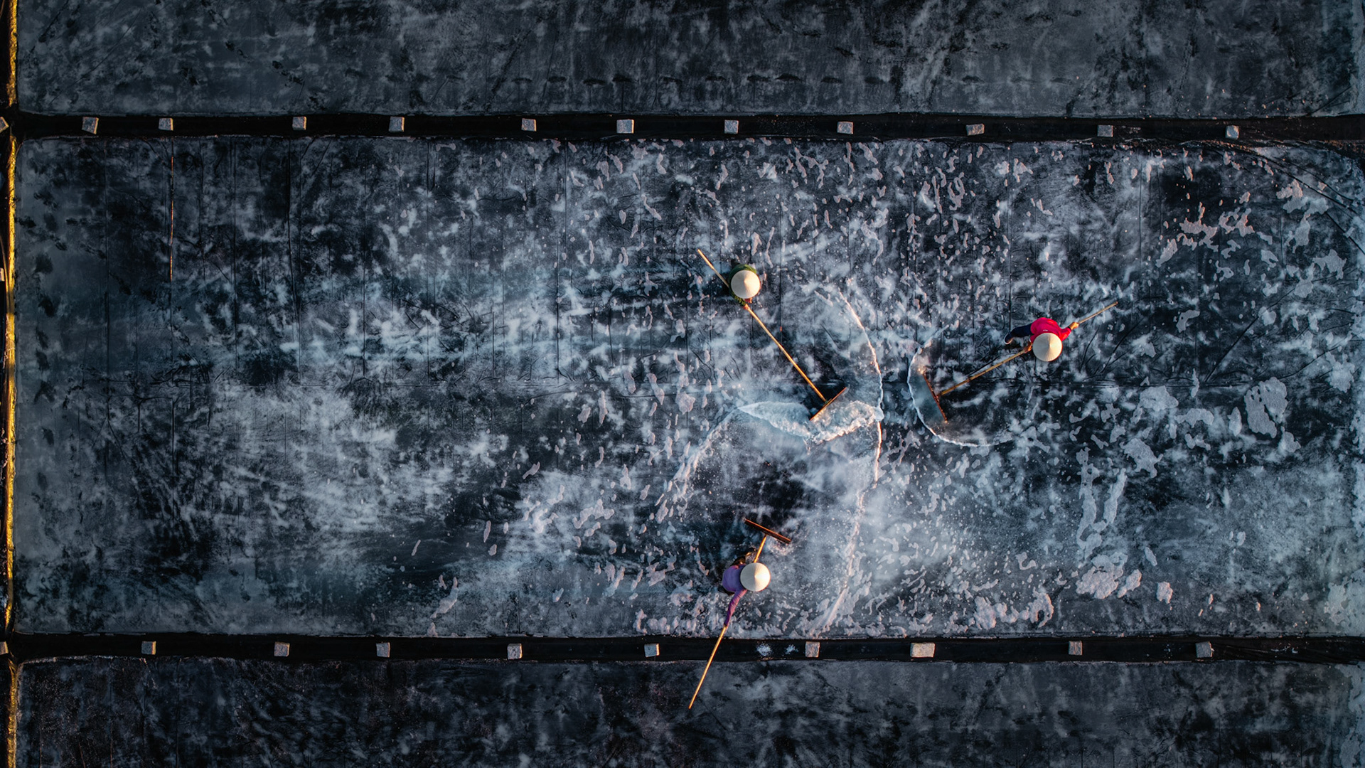 White crystalline pyramids rise from the dark earth, captured from above during the Vietnamese salt harvest.