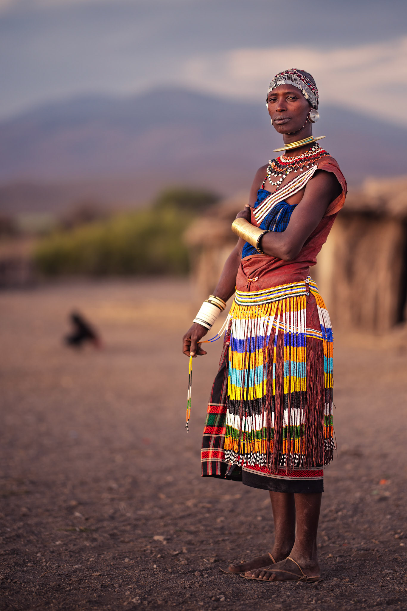 Guardian of Heritage — A striking environmental portrait showing the traditional leather dress, often treated to have a reddish hue, which distinguishes the Datoga. She stands tall as a pillar of her culture, her presence commanding respect against the backdrop of the African sky.