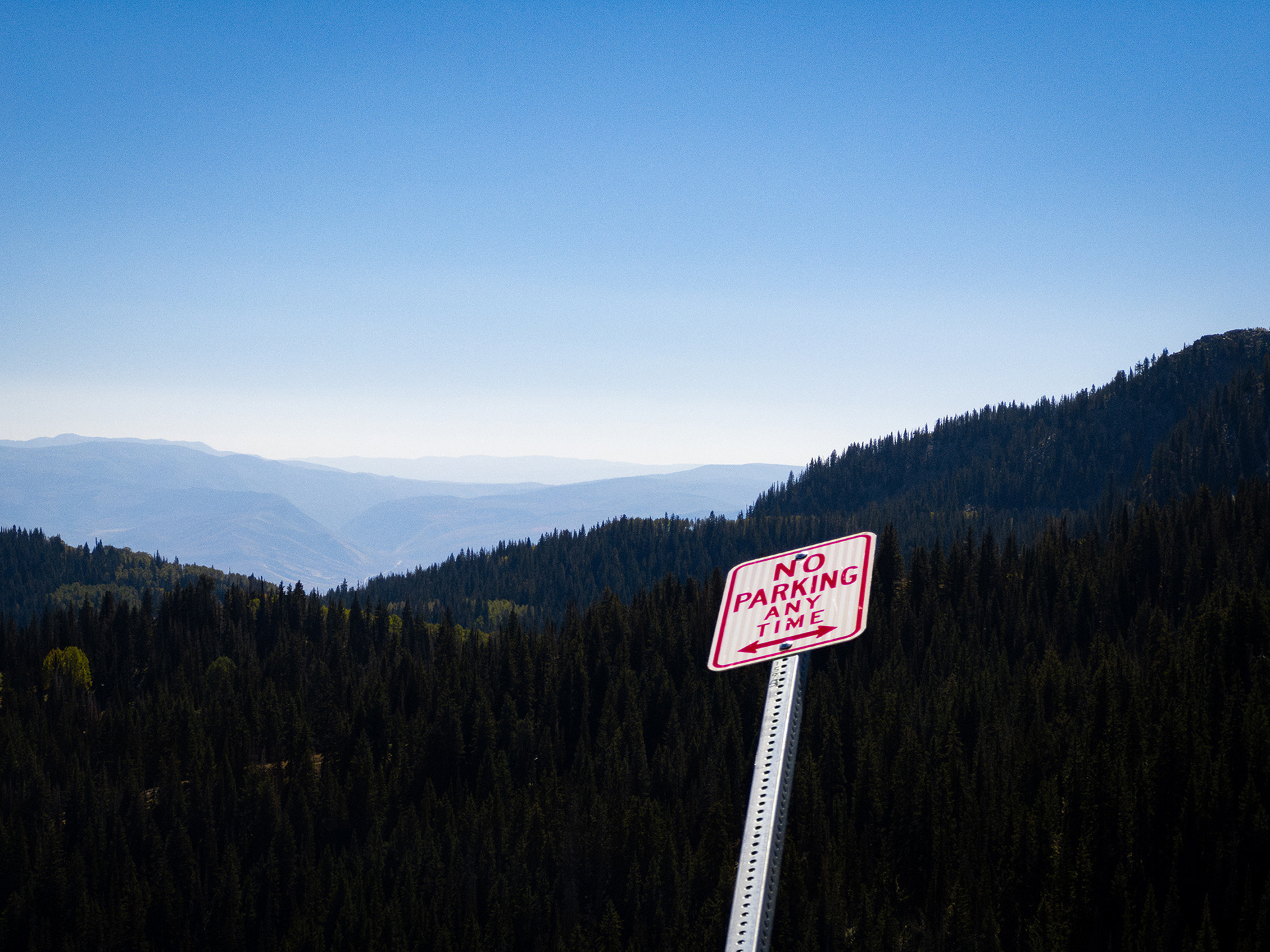 a photograph of a landscape of trees and hills, with a "no parking" sign in the foreground