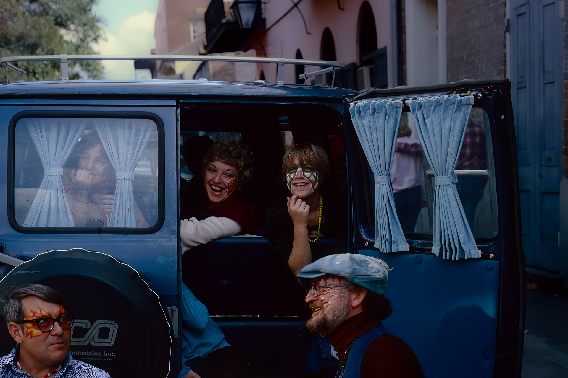A group of face painted revelers sitting in the back of a van from Mardi Gras in New Orleans from the 1970’s