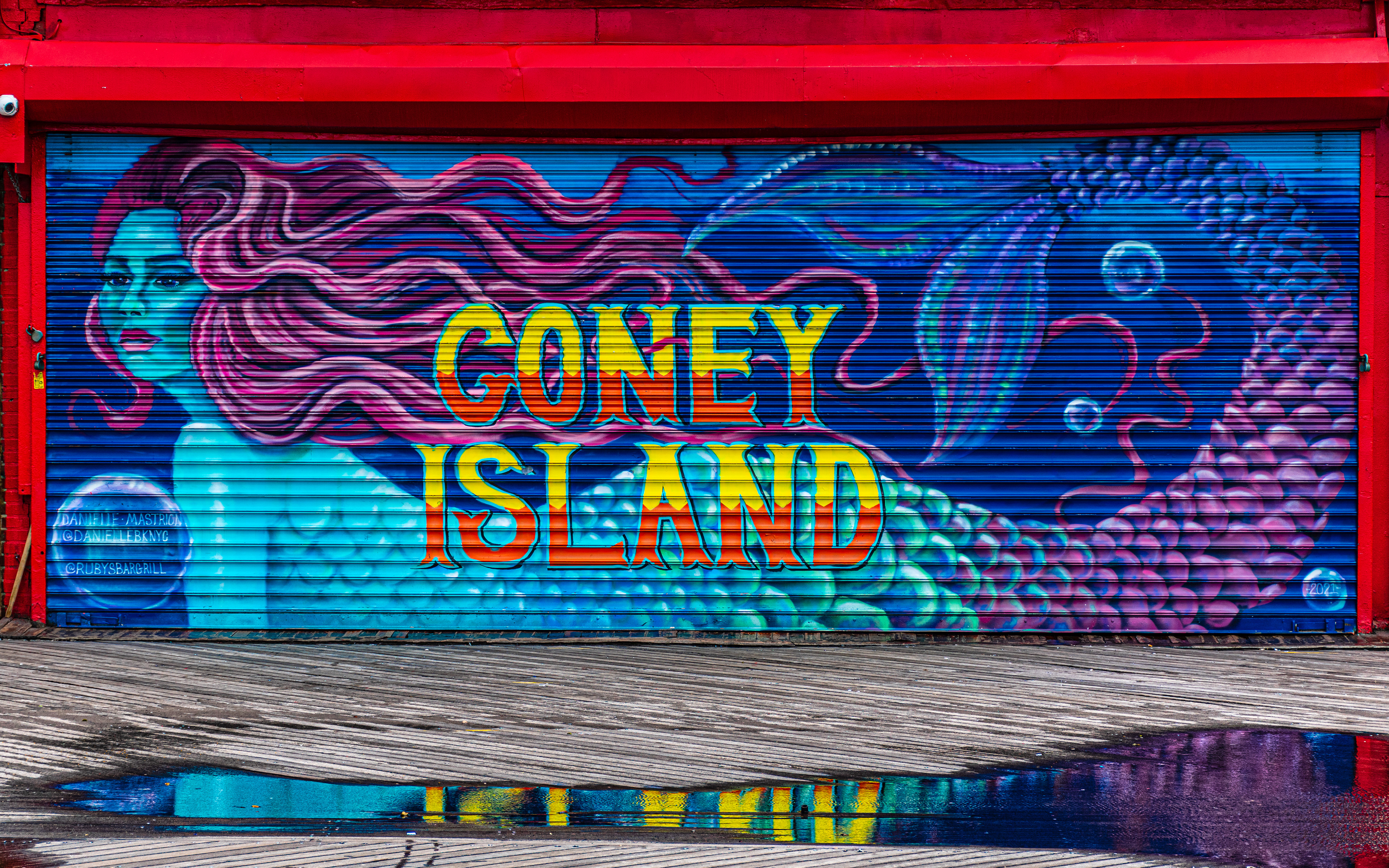 Reflections on the restored “Coney Island” lettering on the gates of Ruby’s Bar and Grill. And Coney island boardwalk’s first mermaid mural painted by Danielle Mastrion