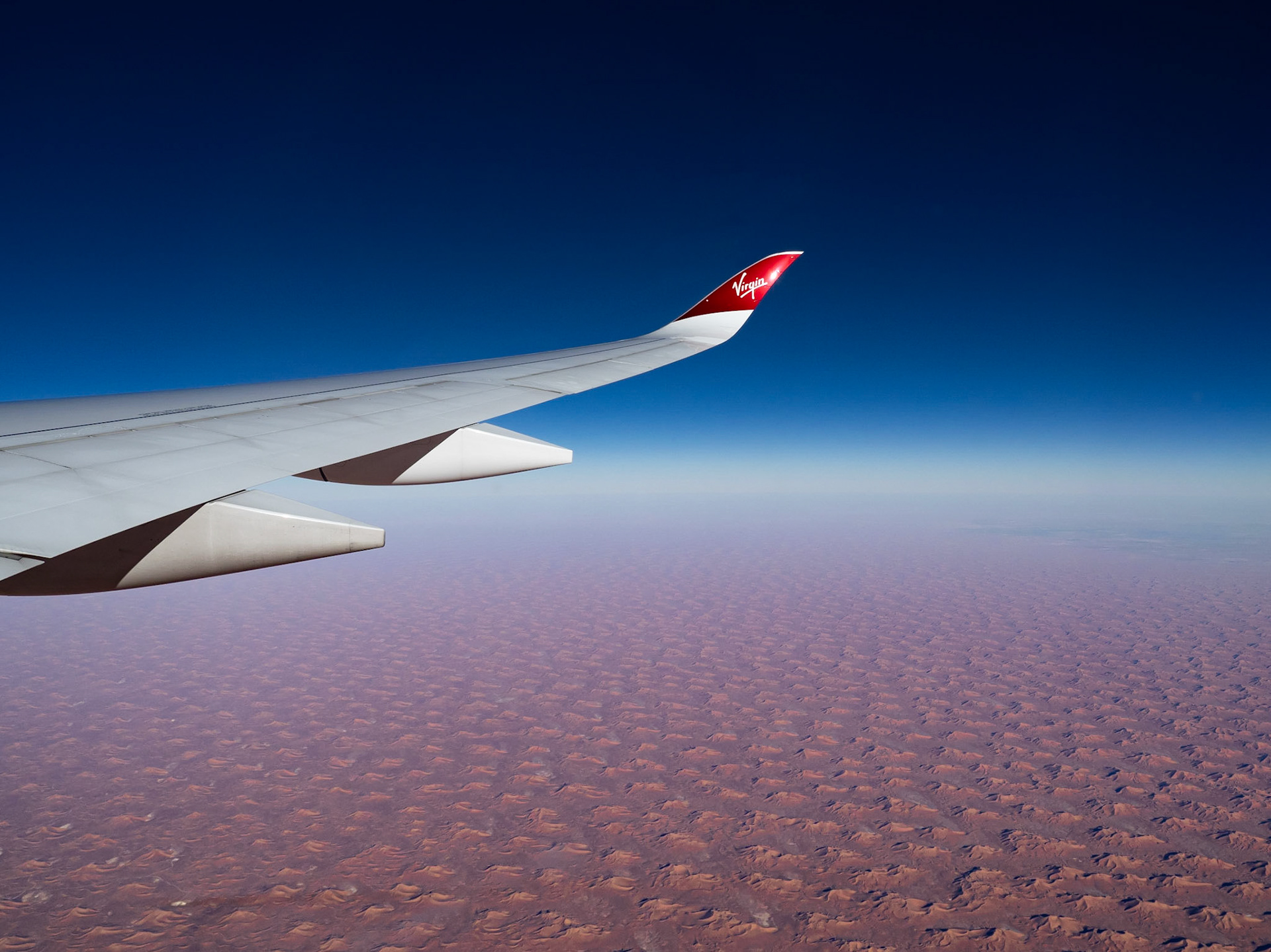 The wingtip of a Virgin Atlantic aircraft as it flies over the dunes of the Sahara desert in Niger