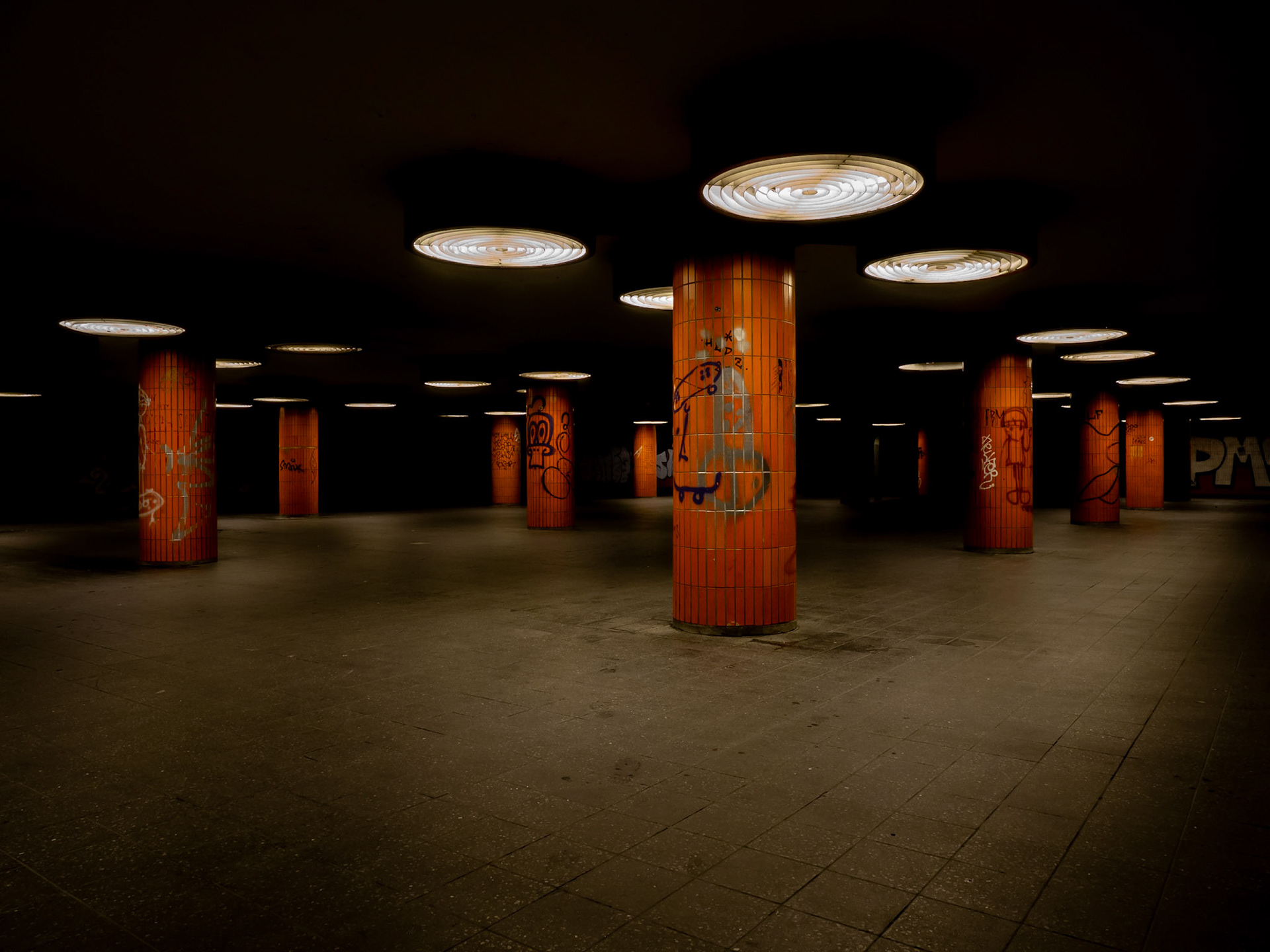 Circular downlights illuminate a gloomy path in a graffiti-ridden underpass in Berlin