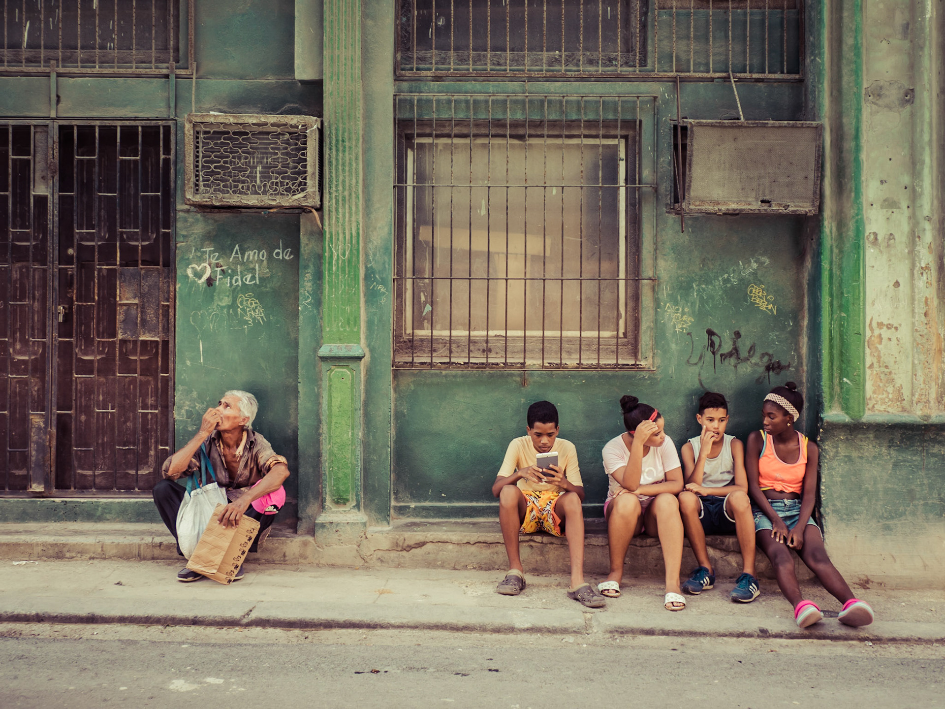 An elderly man contemplates whilst his younger neighbours entertain themselves using more modern technology, a rarity in Havana