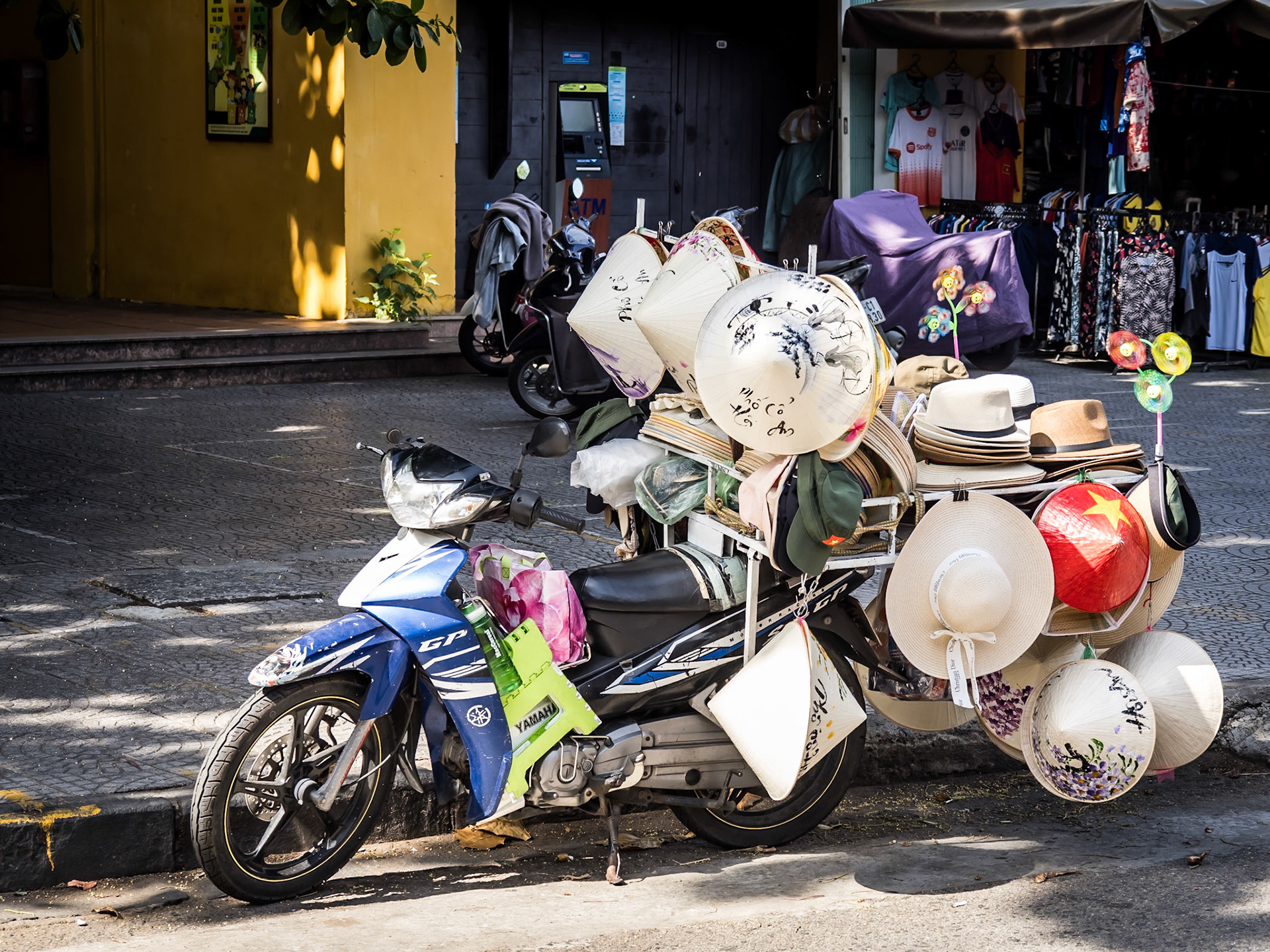 A vast collection of Non La 'Leaf' and other hats sits precariously on the back of a trusty scooter by the market building in Hoi An